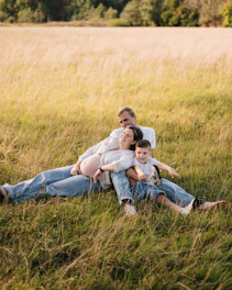 A family sitting in a sunlit grassy field, two adults and a child