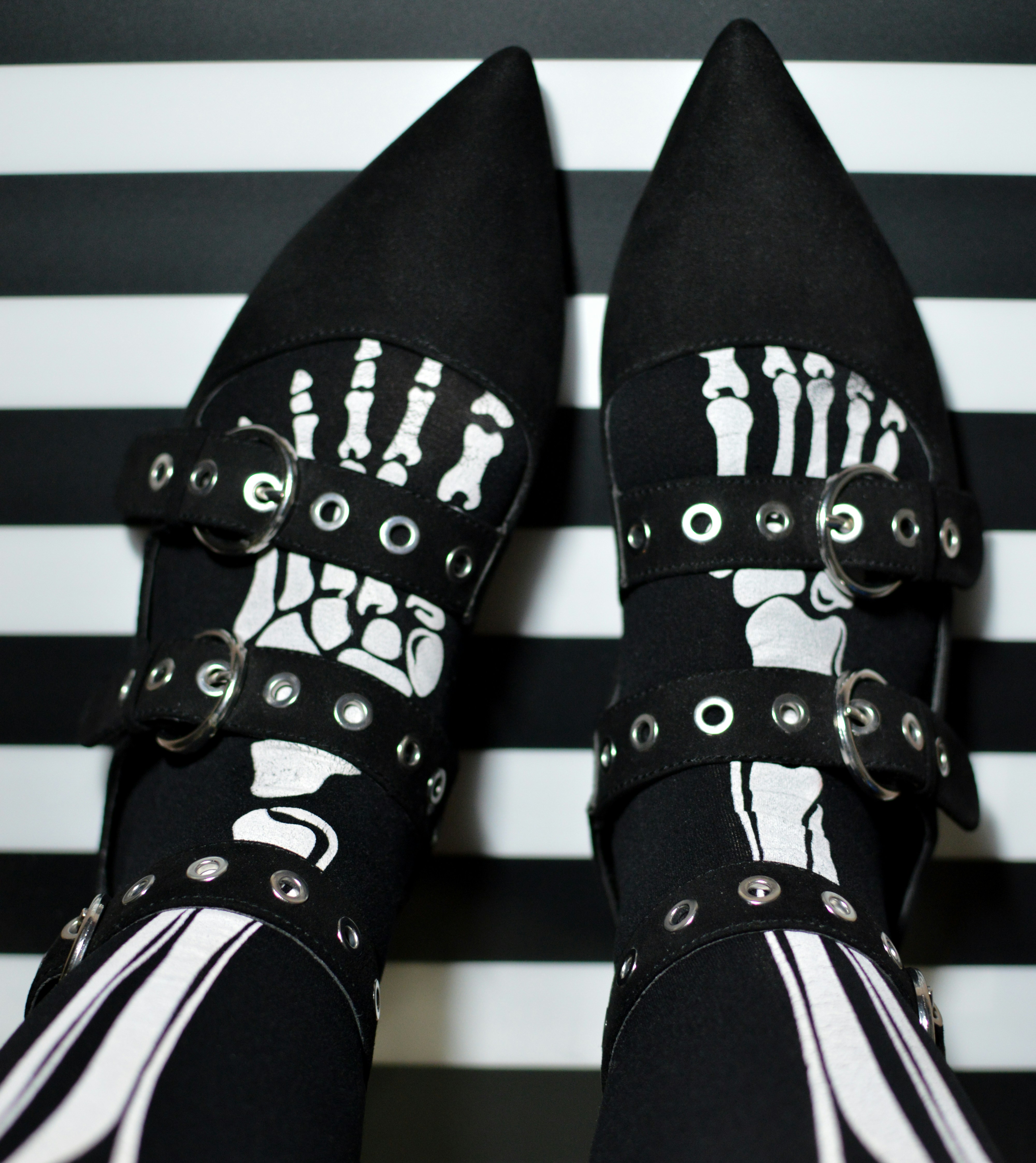 Black pointed shoes with white skeleton foot prints on a black and white striped background