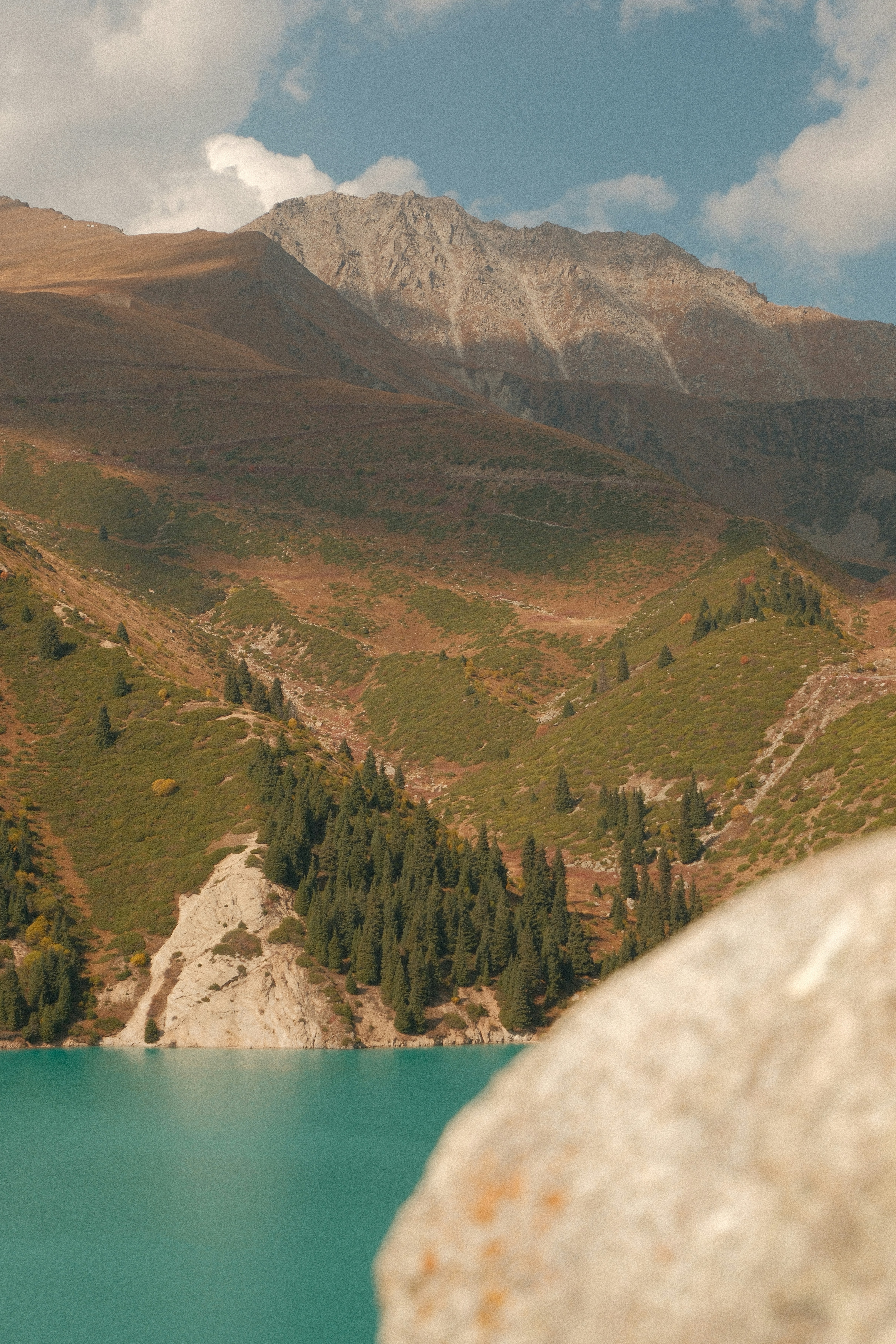 Turquoise lake water below green mountain slopes with pine trees and rocky peaks