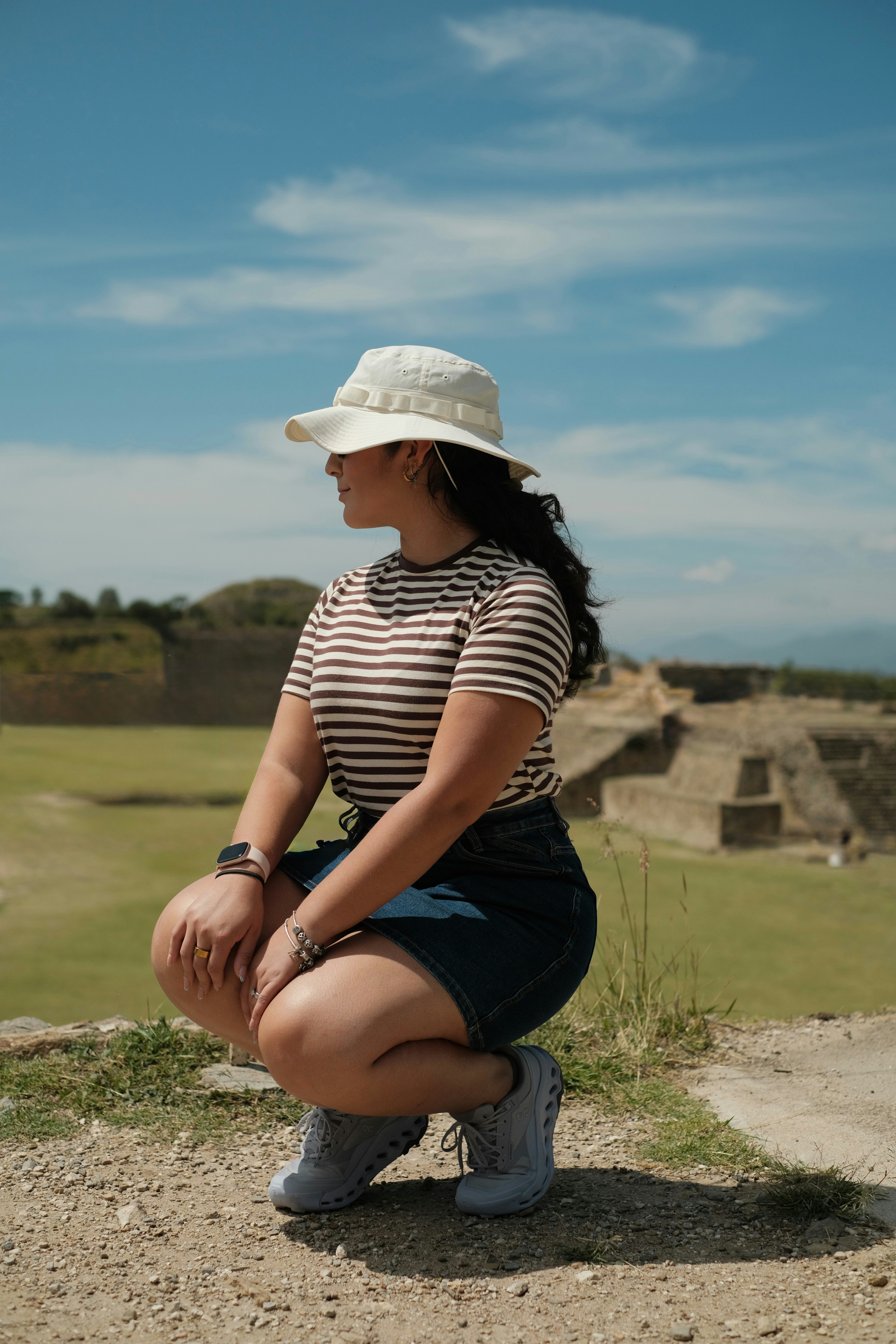 Una mujer con sombrero tipo cubo y camisa a rayas agachada en un yacimiento arqueológico