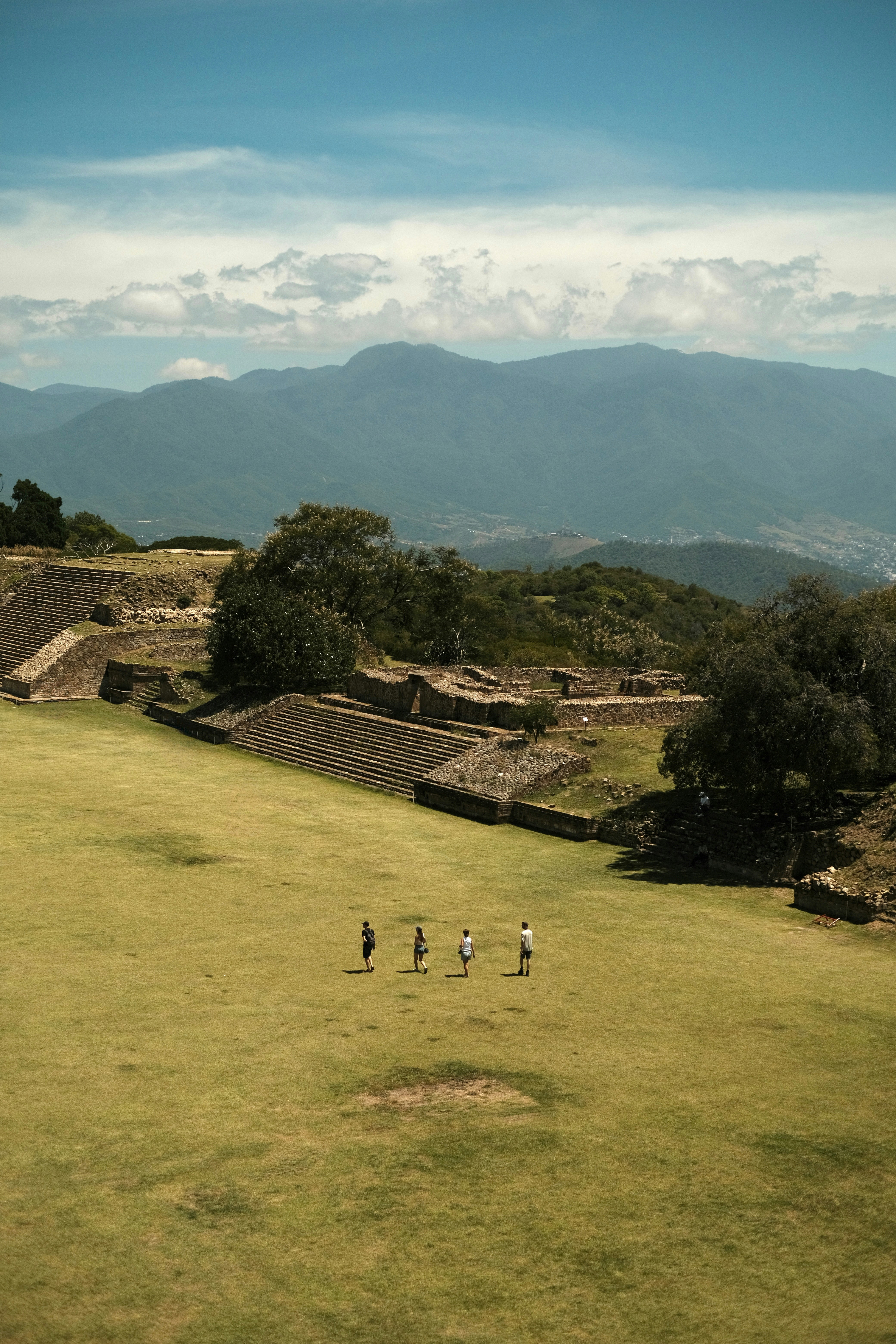 Cuatro personas caminando por una plaza cubierta de césped en las ruinas del Monte Albán