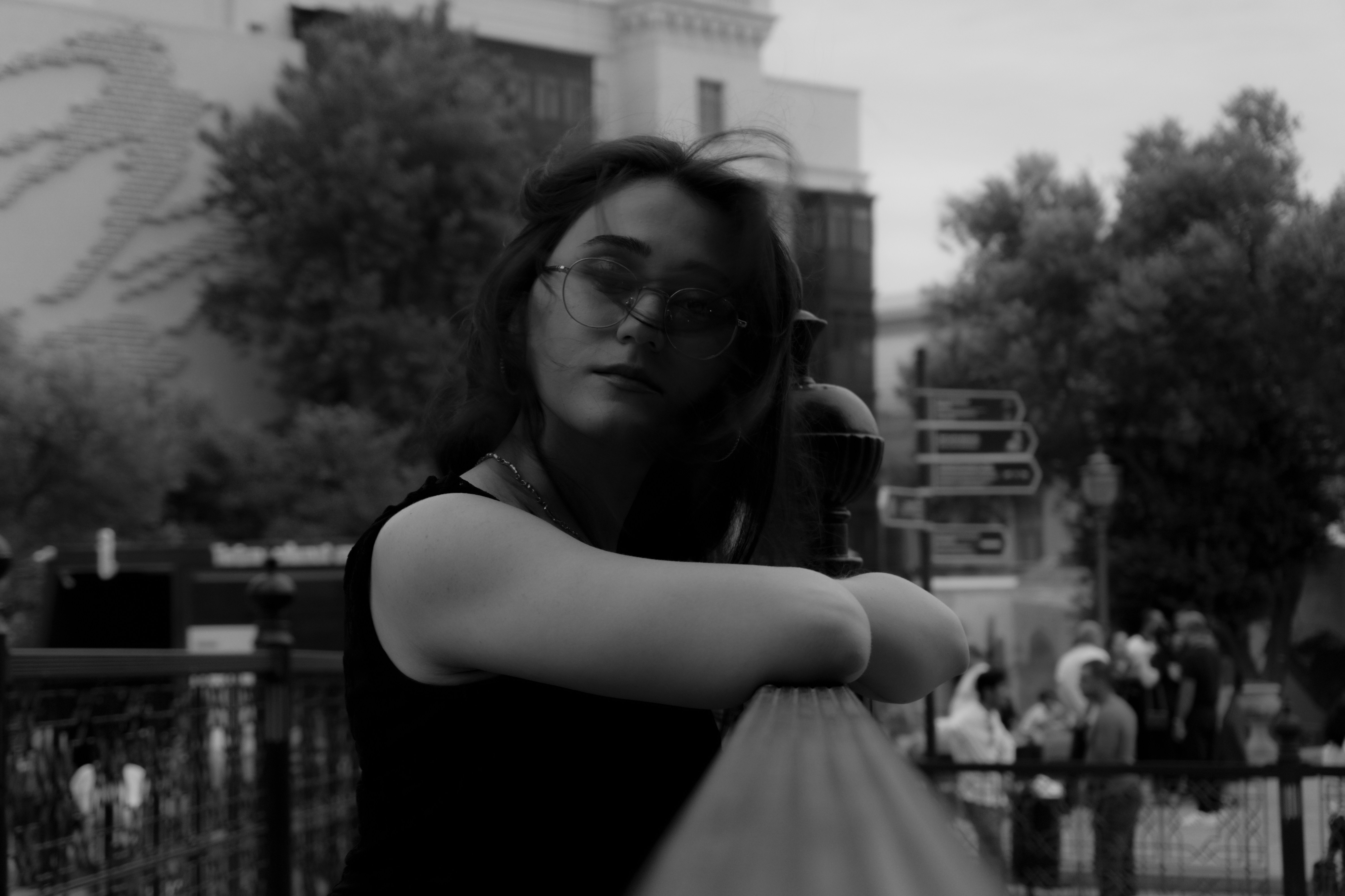 A woman with glasses leaning on a railing in a public square