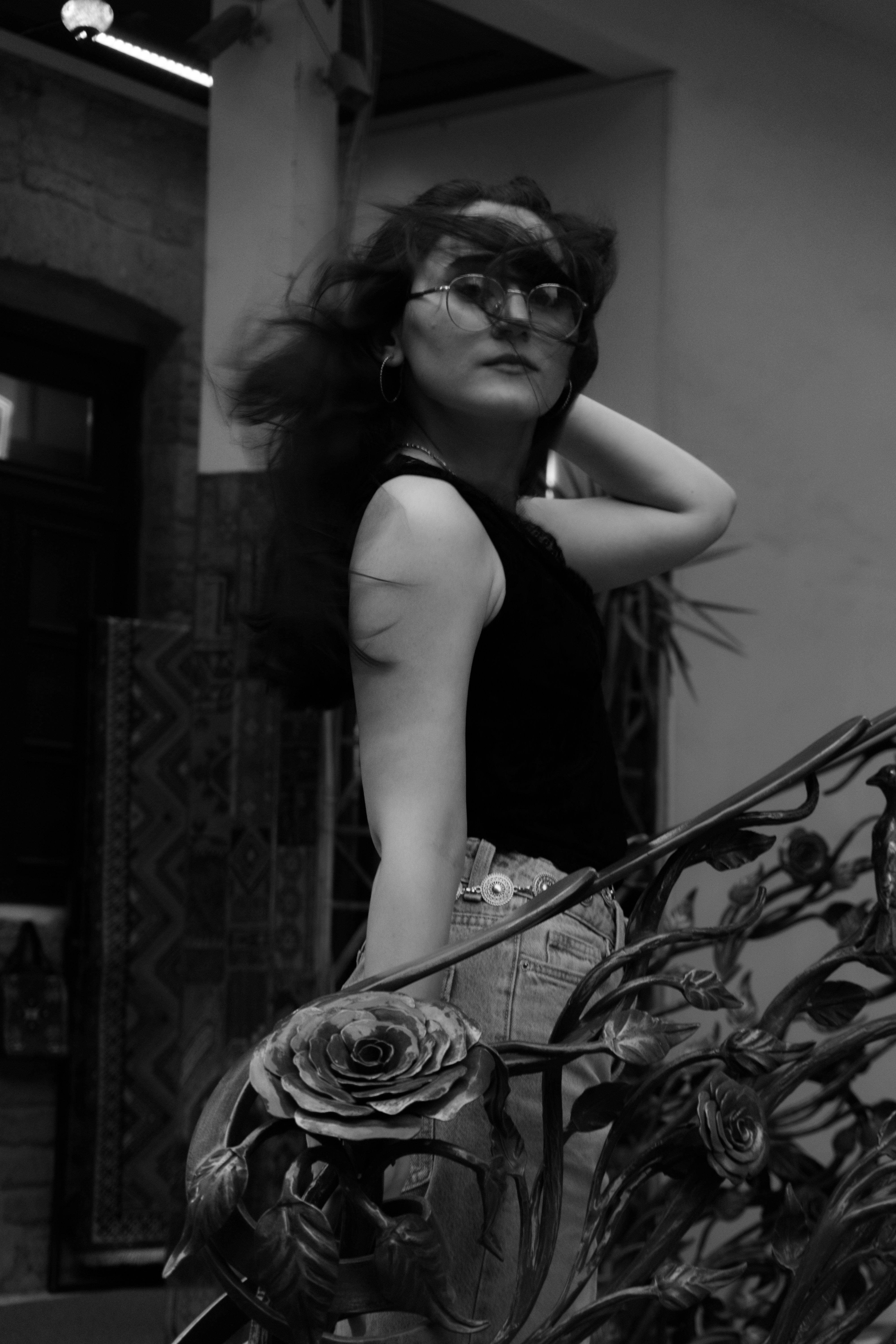 A woman with windblown hair standing by a metal railing with rose ornaments