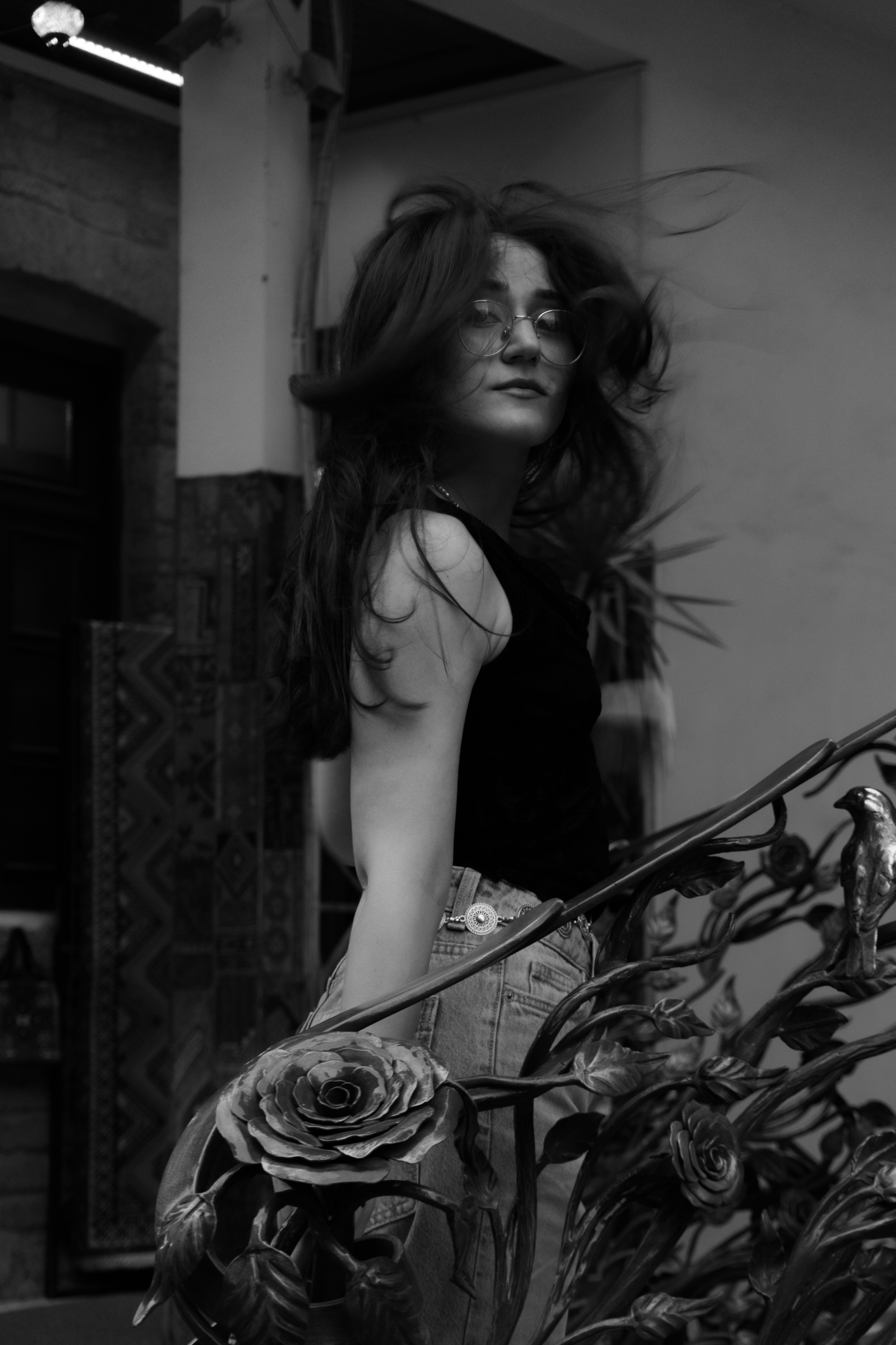 A woman with long hair and glasses leaning on a decorative metal railing