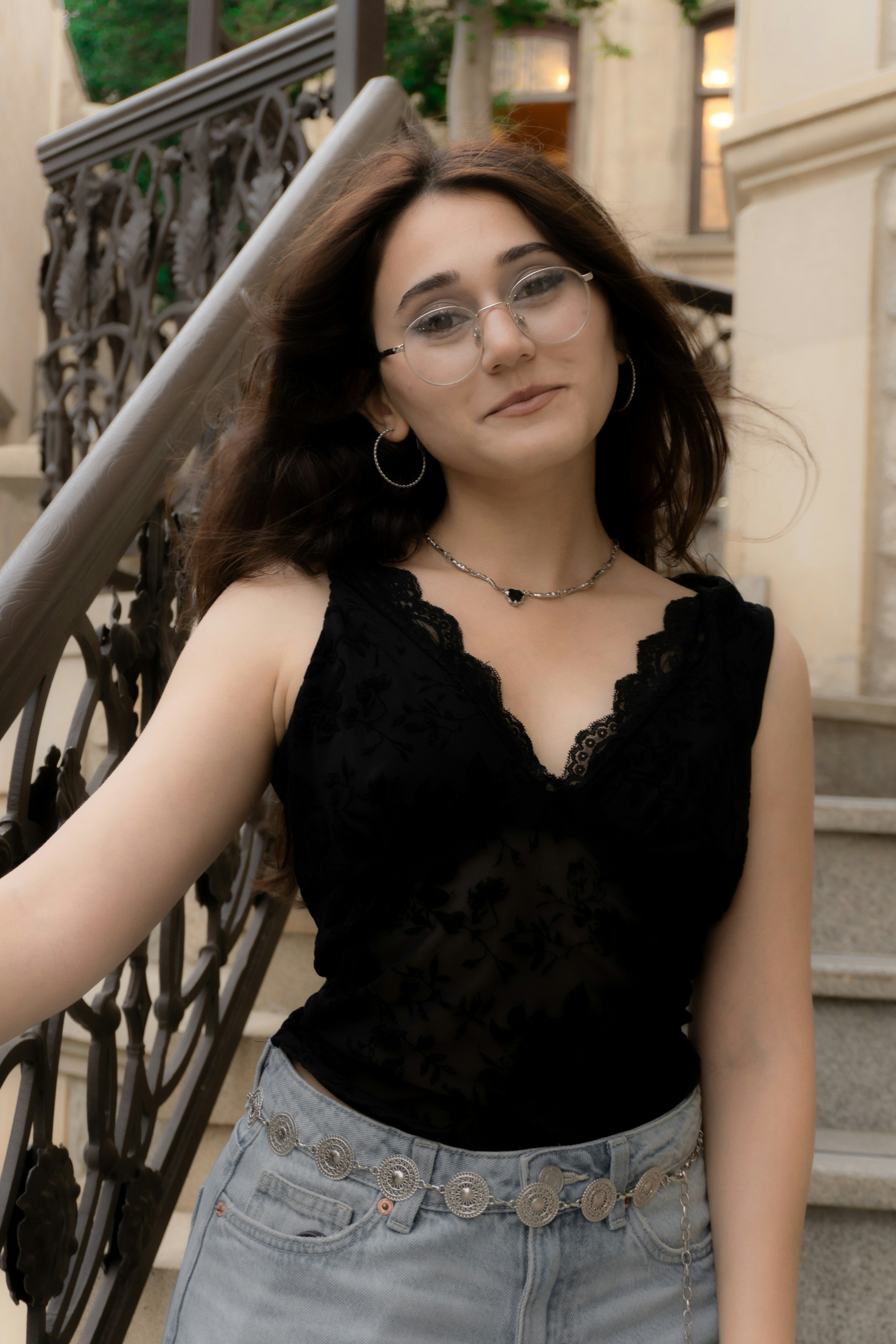 A young woman with glasses and a black lace top on stone stairs