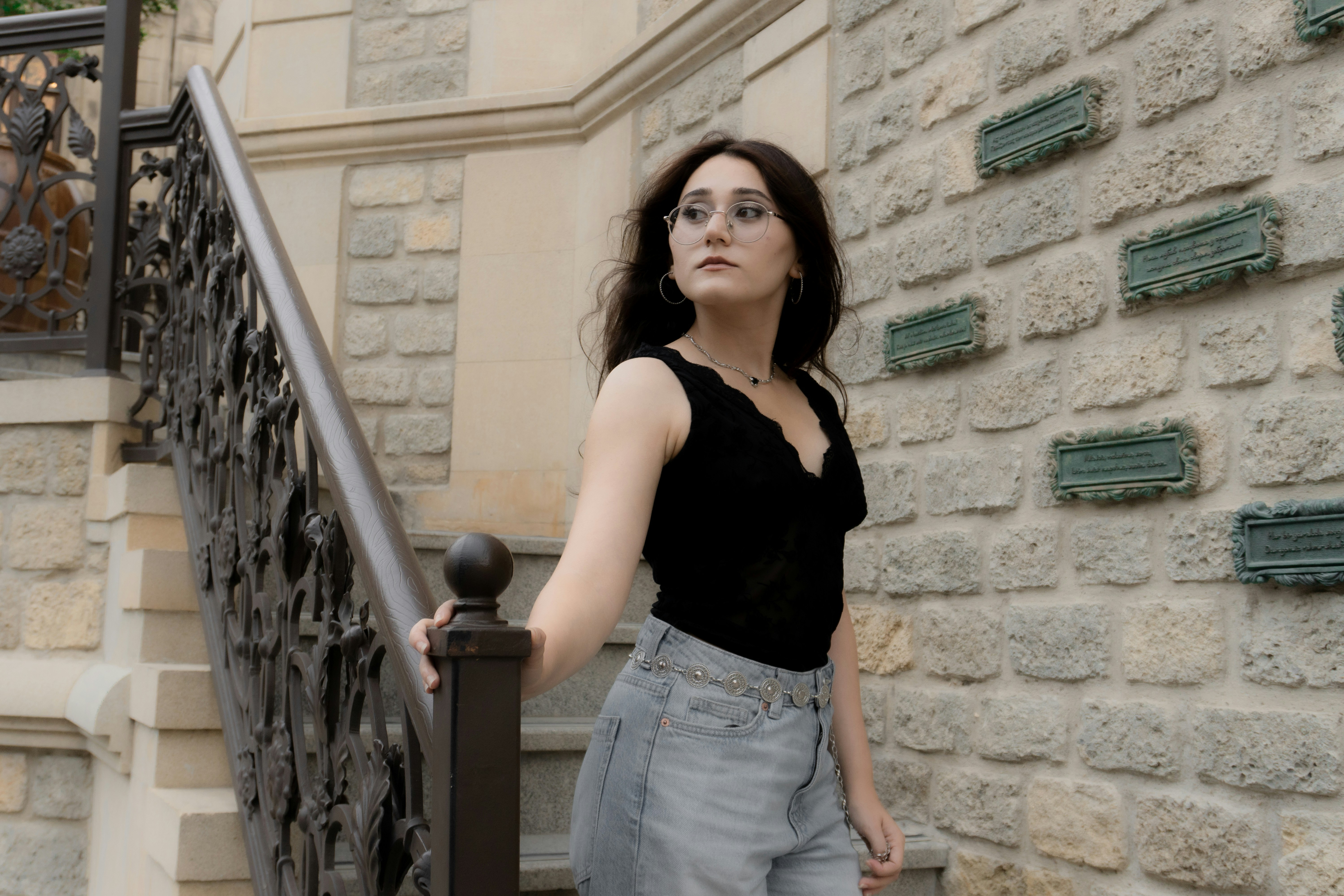 A woman in a black top and jeans on stone stairs with a railing