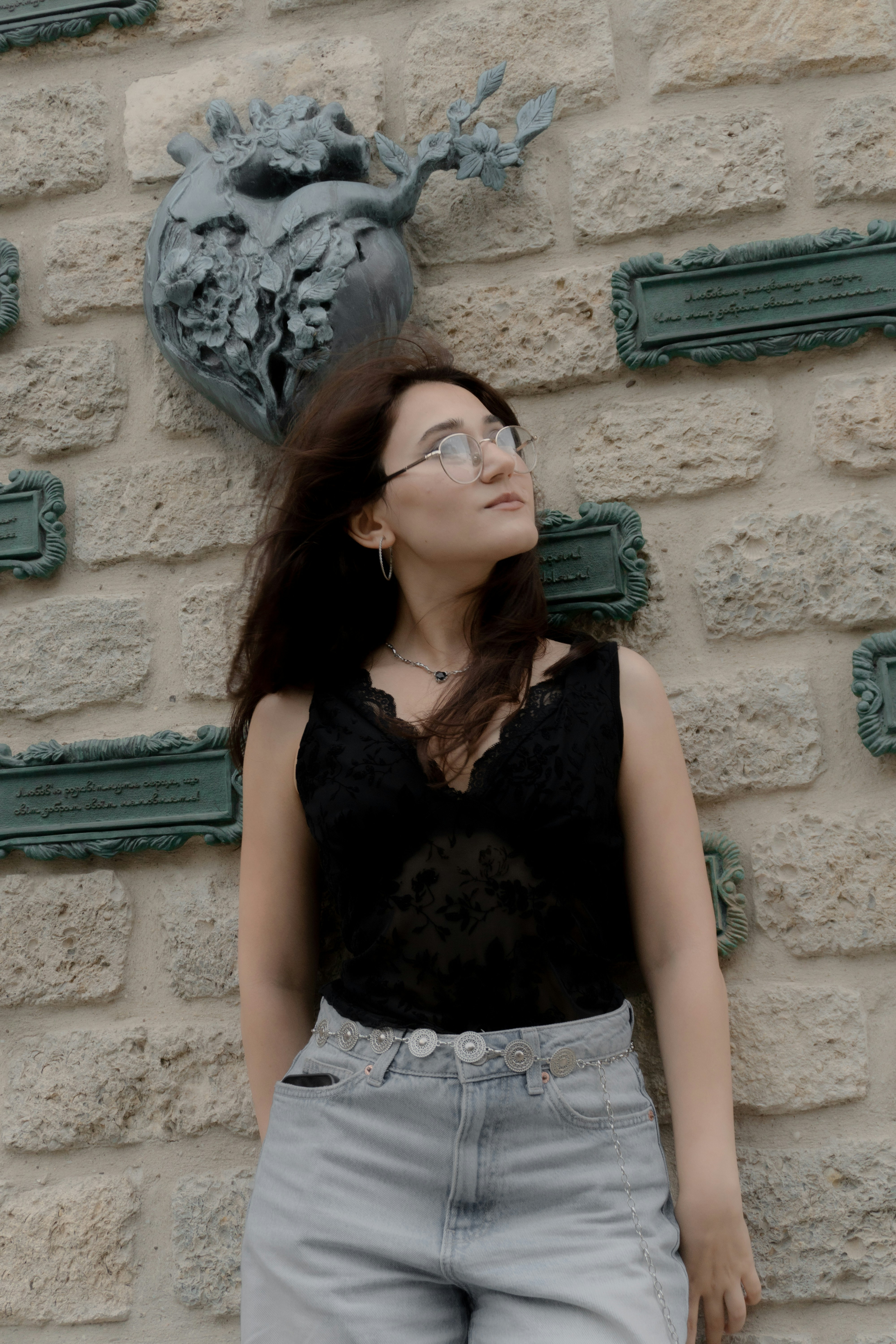 A woman in a black lace top and jeans against a stone wall
