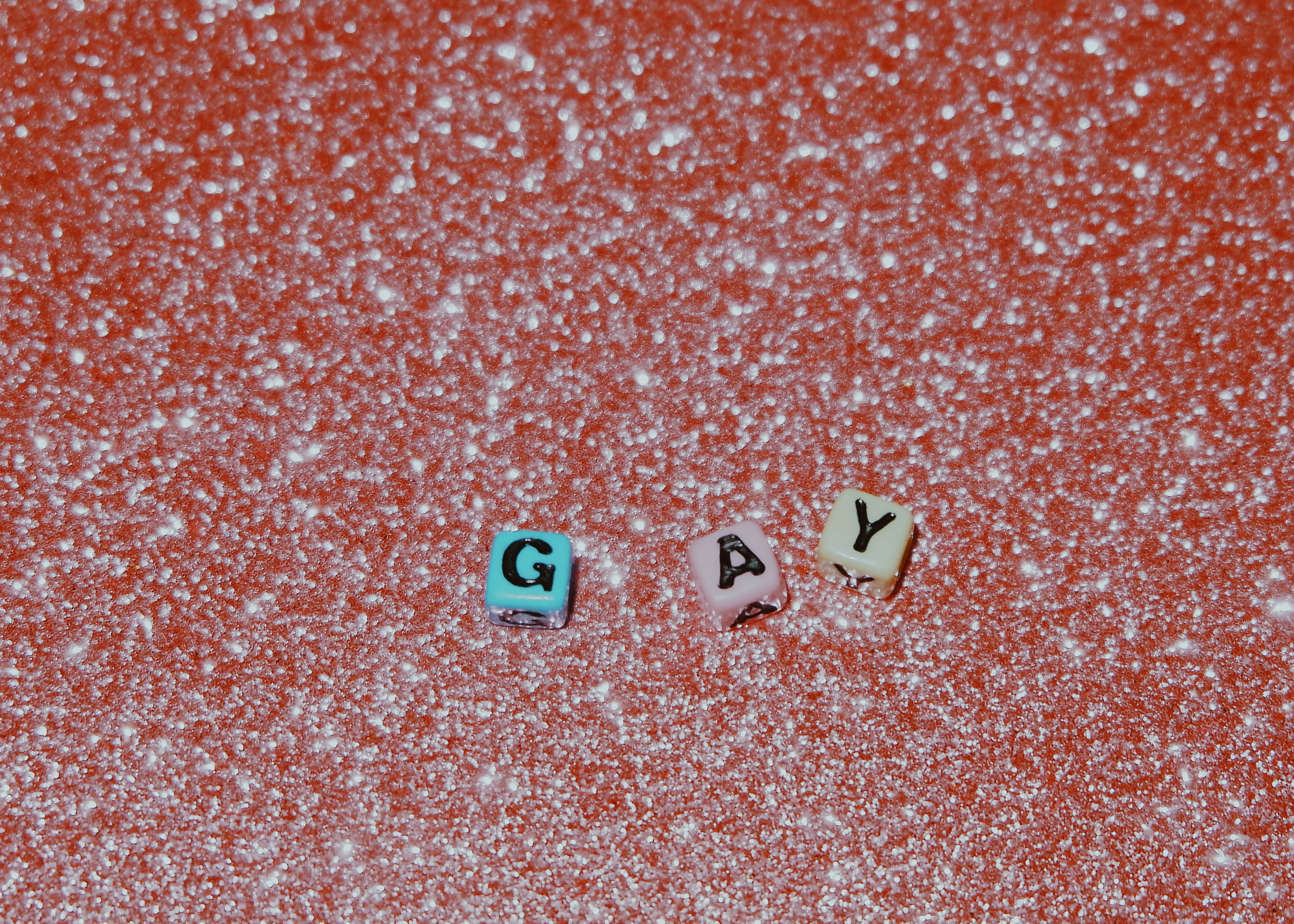 Three letter beads spelling "GAY" on a sparkling red surface - 相关推荐