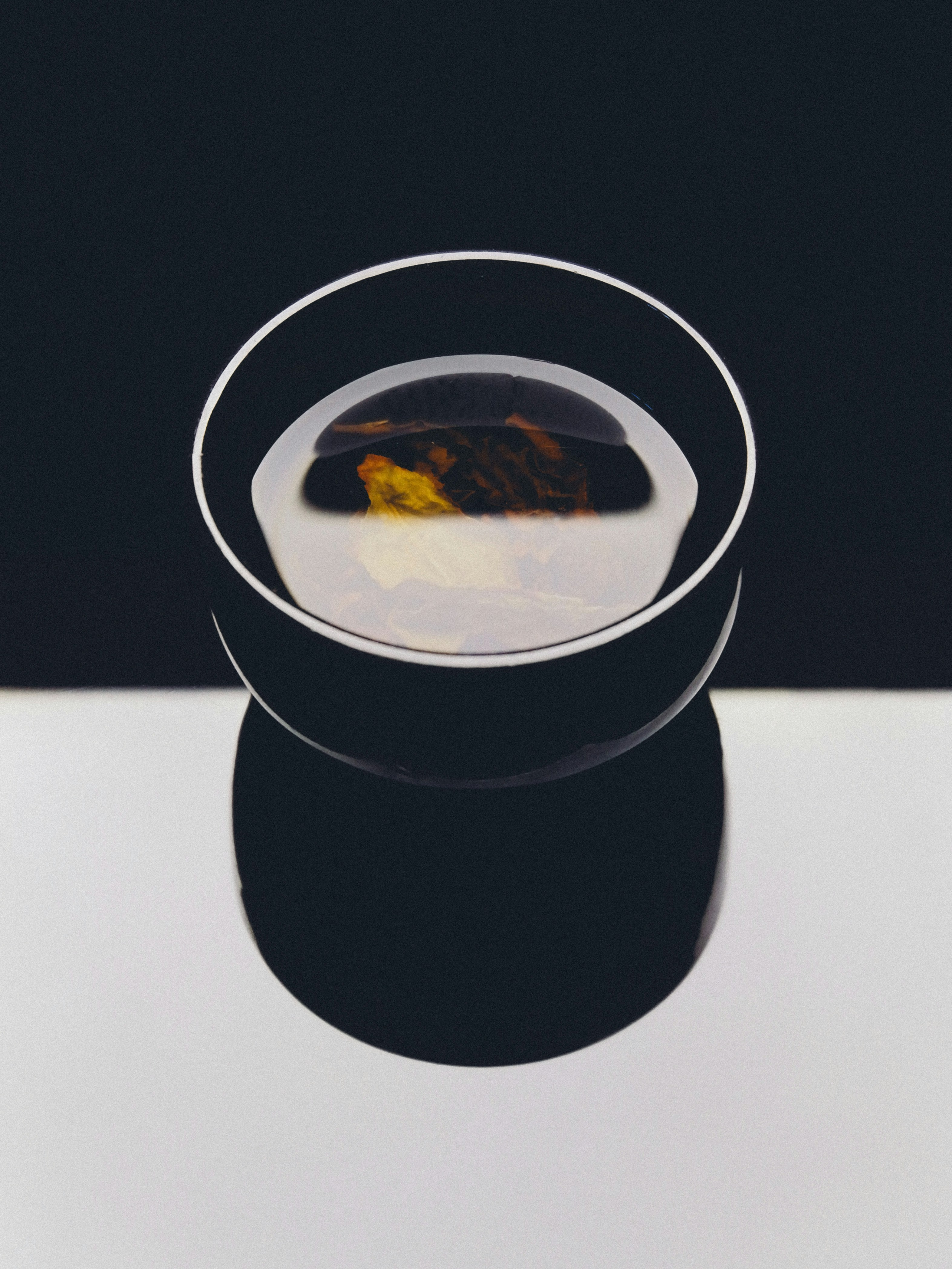 A black bowl of tea with floating leaves on a white surface
