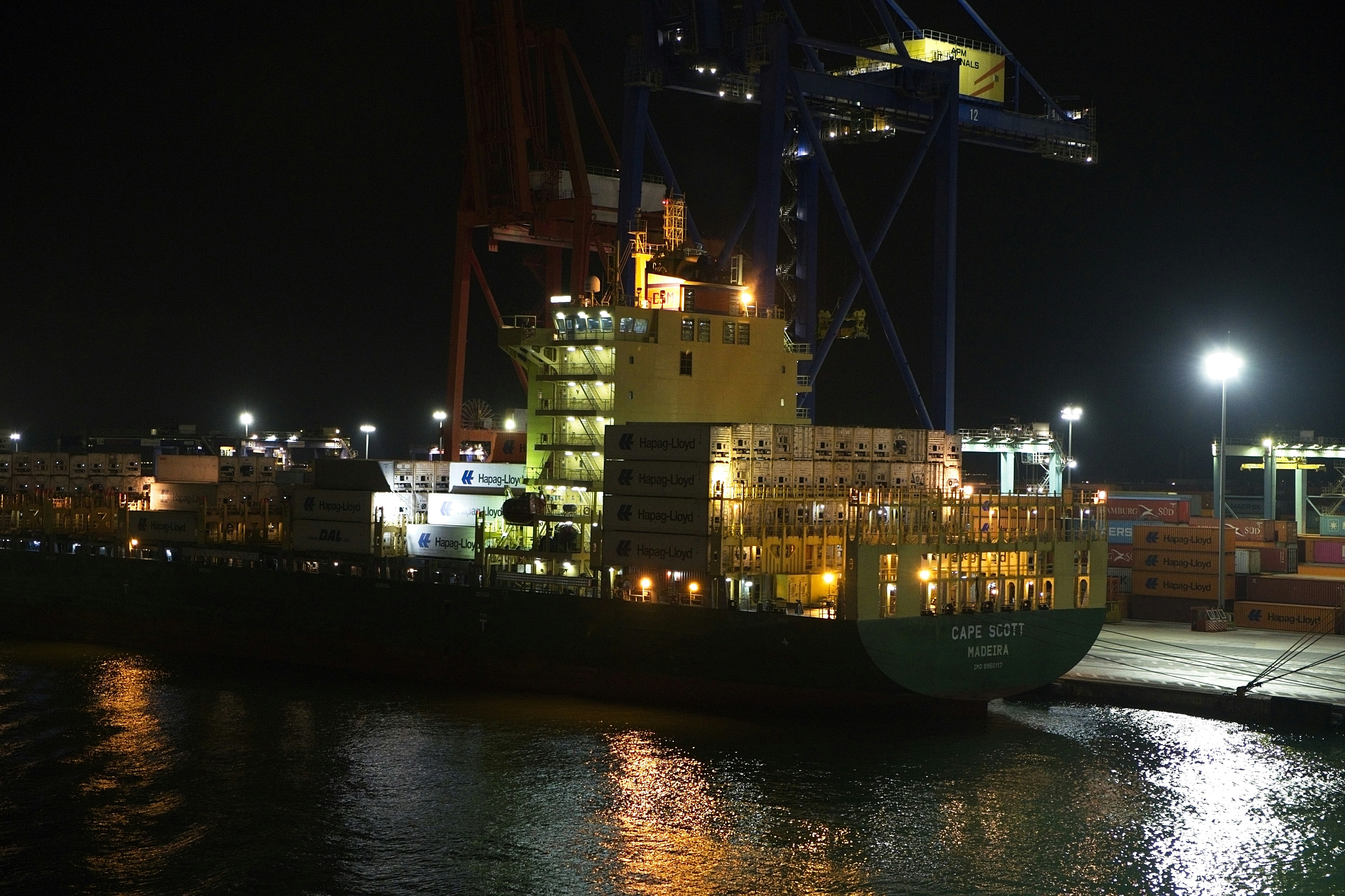 A container ship docked at a port at night under bright floodlights