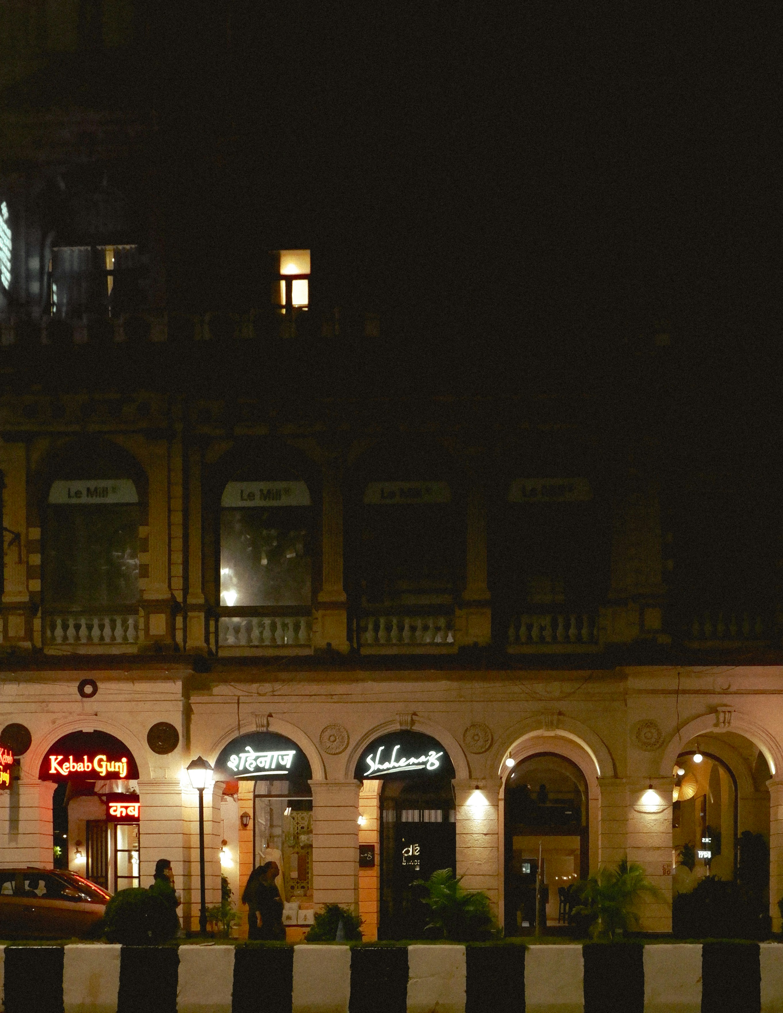 Illuminated storefronts with arched windows and neon signs at night in Mumbai