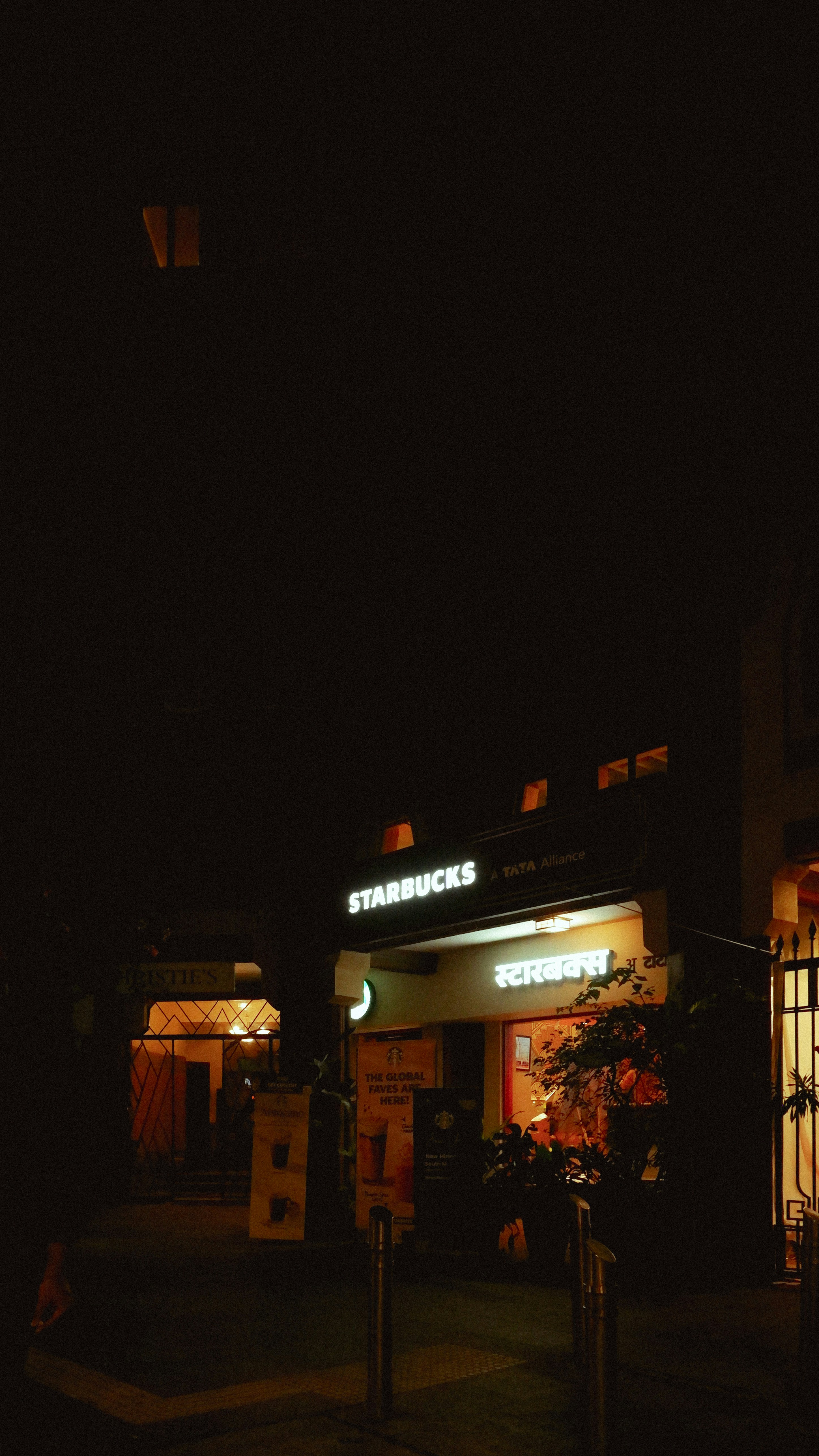 A Starbucks storefront with illuminated signs in English and Hindi at night