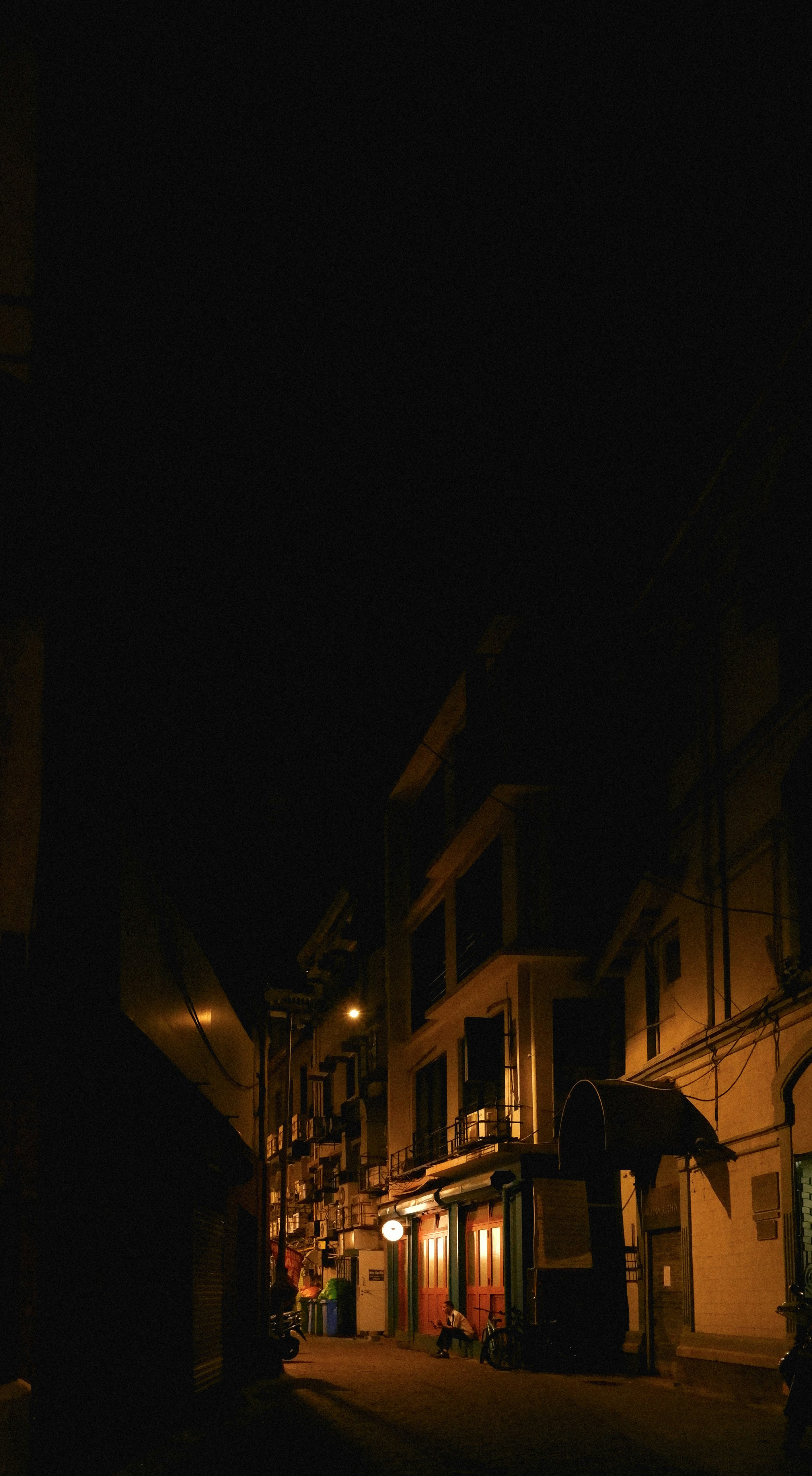 A person sitting on a quiet street at night illuminated by warm streetlights
