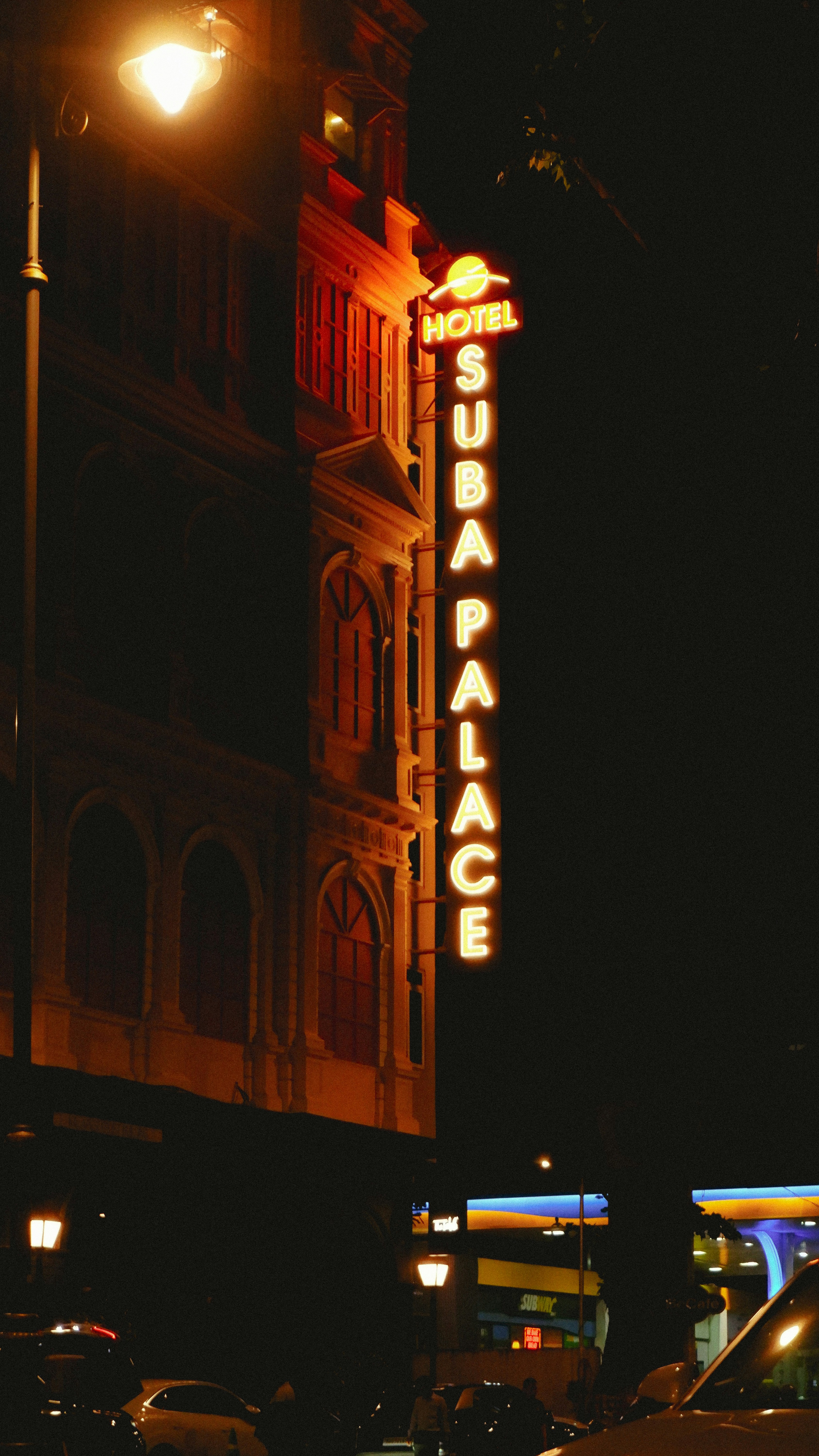 A vertical neon sign reading "HOTEL SUBA PALACE" on a building at night