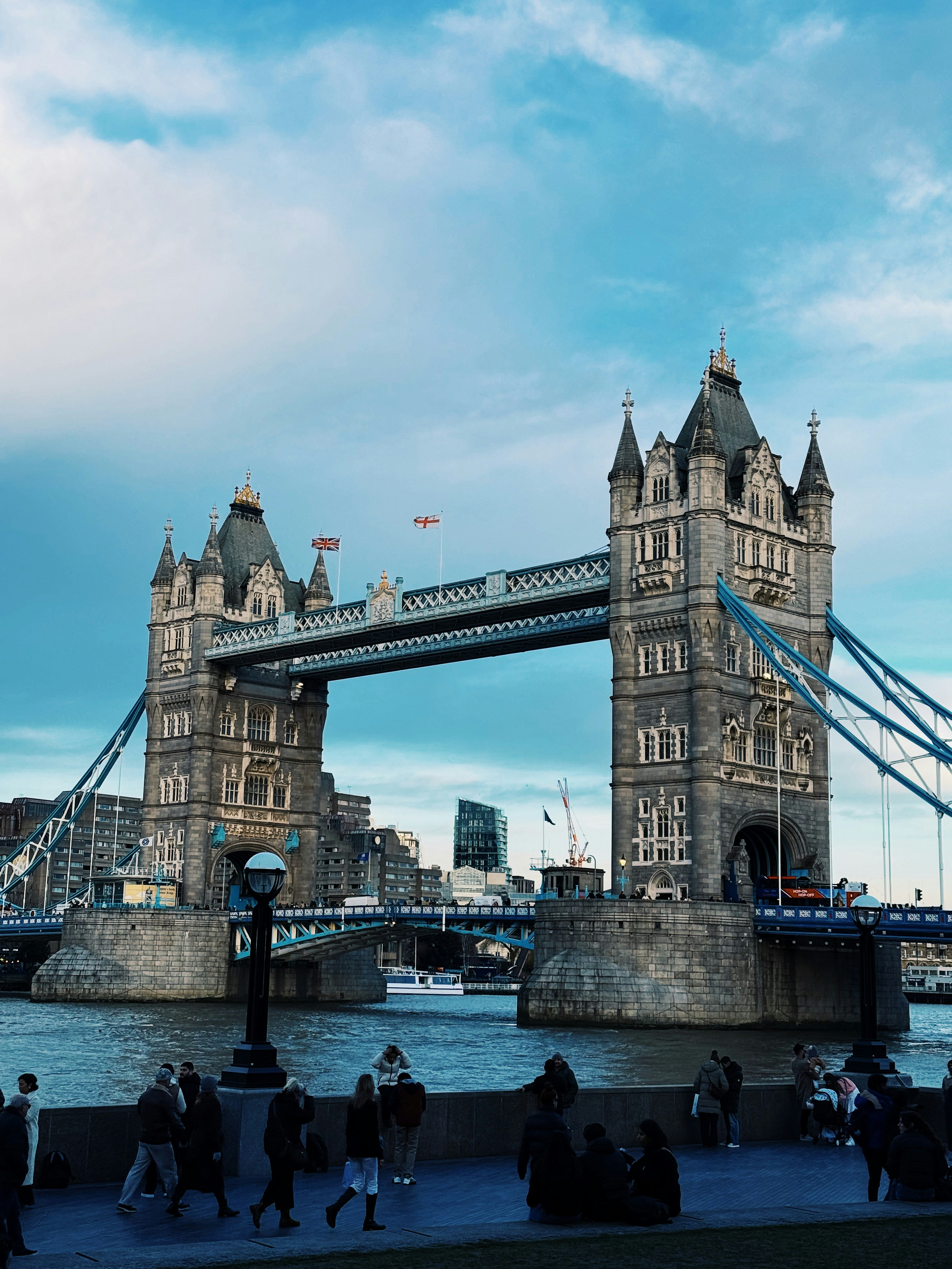 Tower Bridge over the River Thames with people walking along the embankment in London