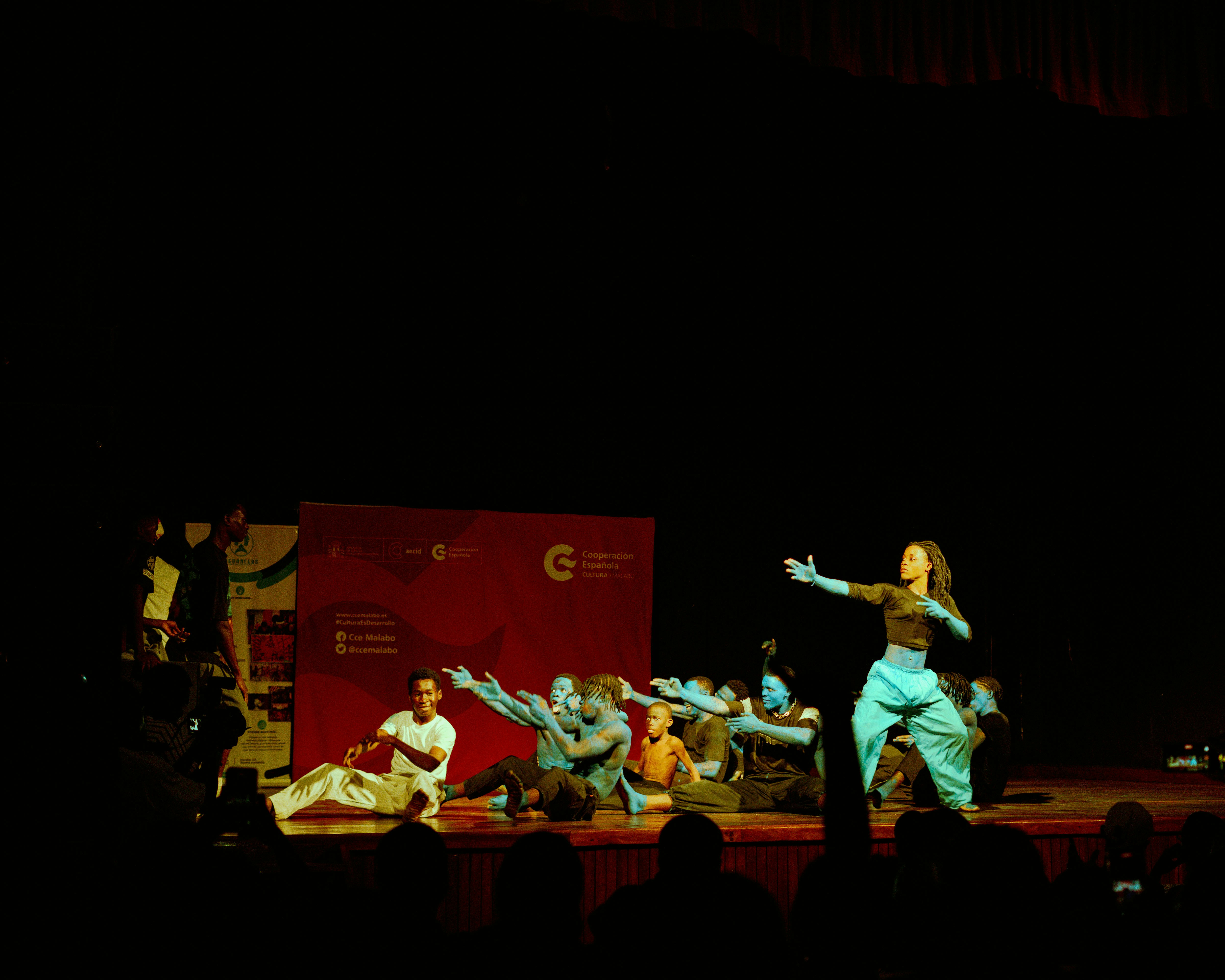 A group of dancers with blue-painted skin performing on a dark stage