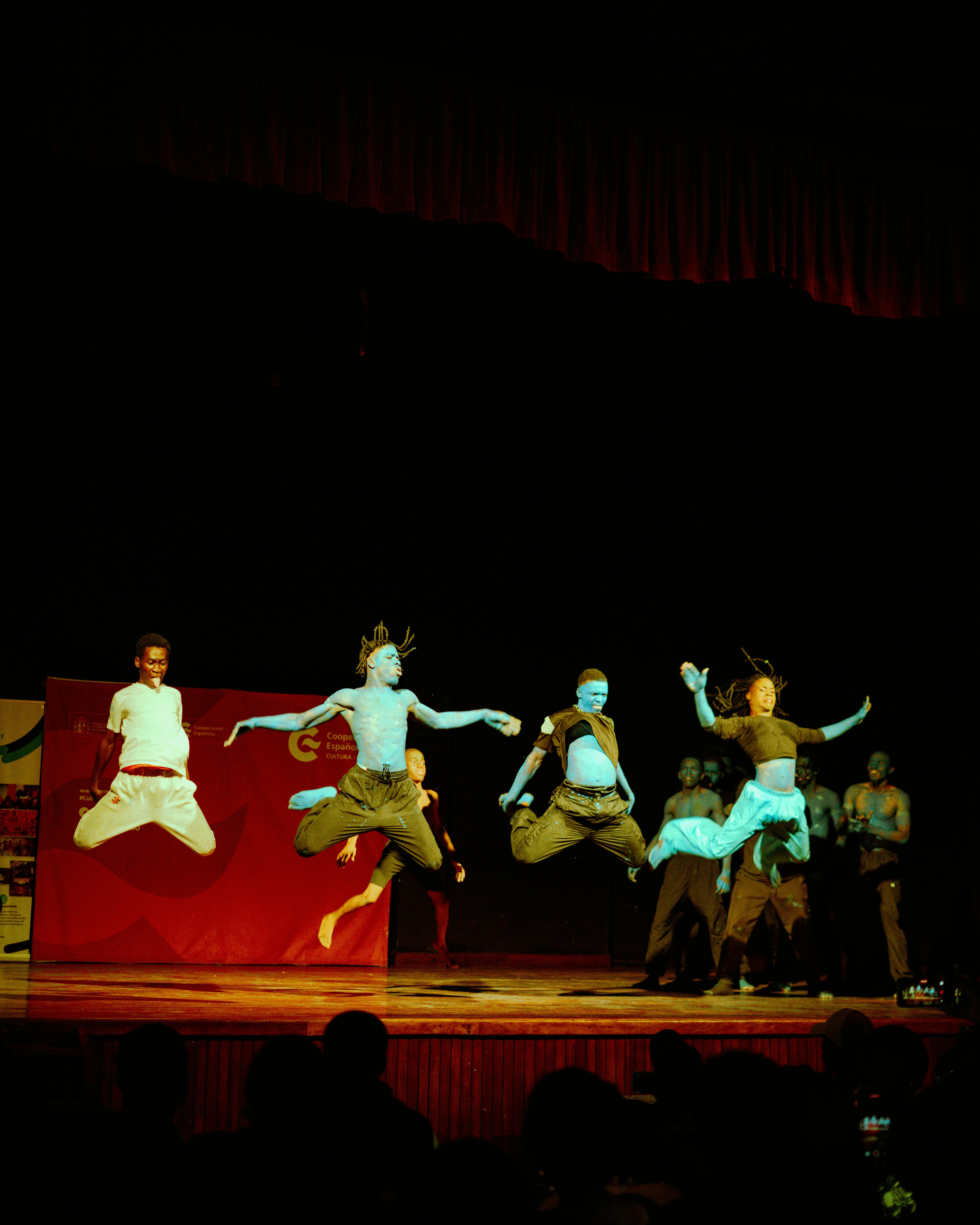 Um grupo de dançarinos pulando em um palco diante de um fundo vermelho