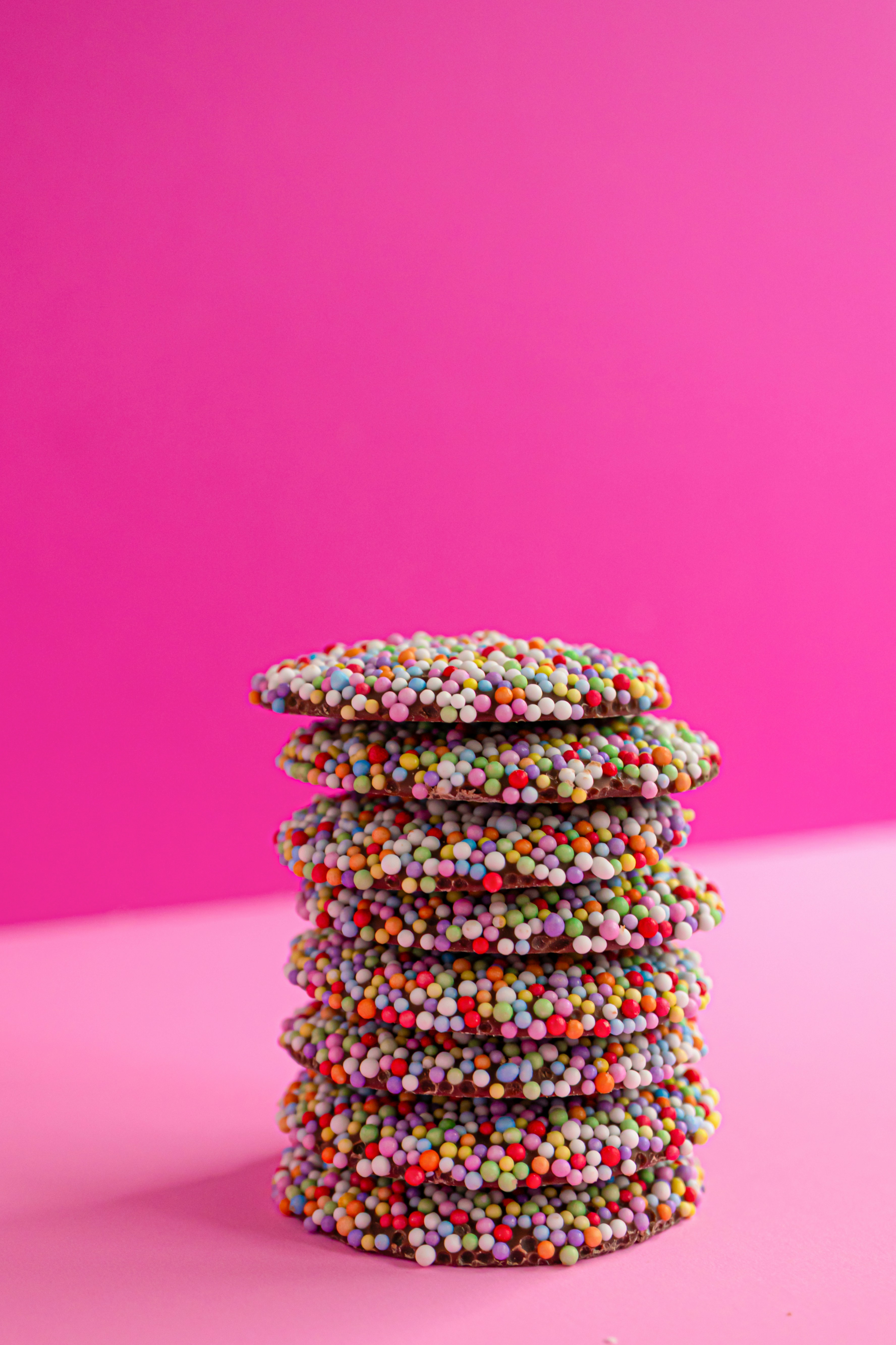 A stack of chocolate cookies covered in colorful sugar sprinkles on a pink surface