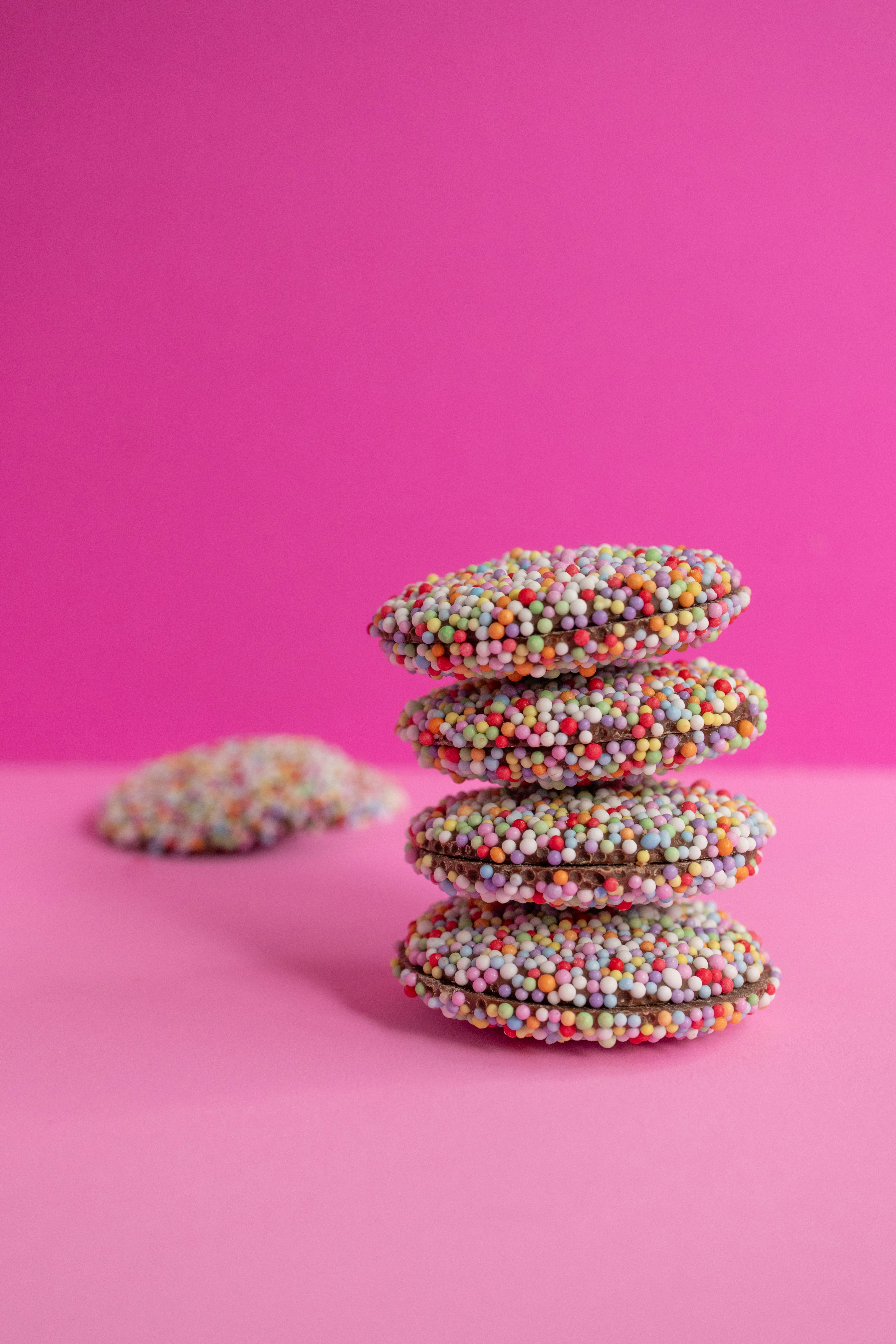 A stack of four chocolate cookies covered in colorful sugar sprinkles on pink