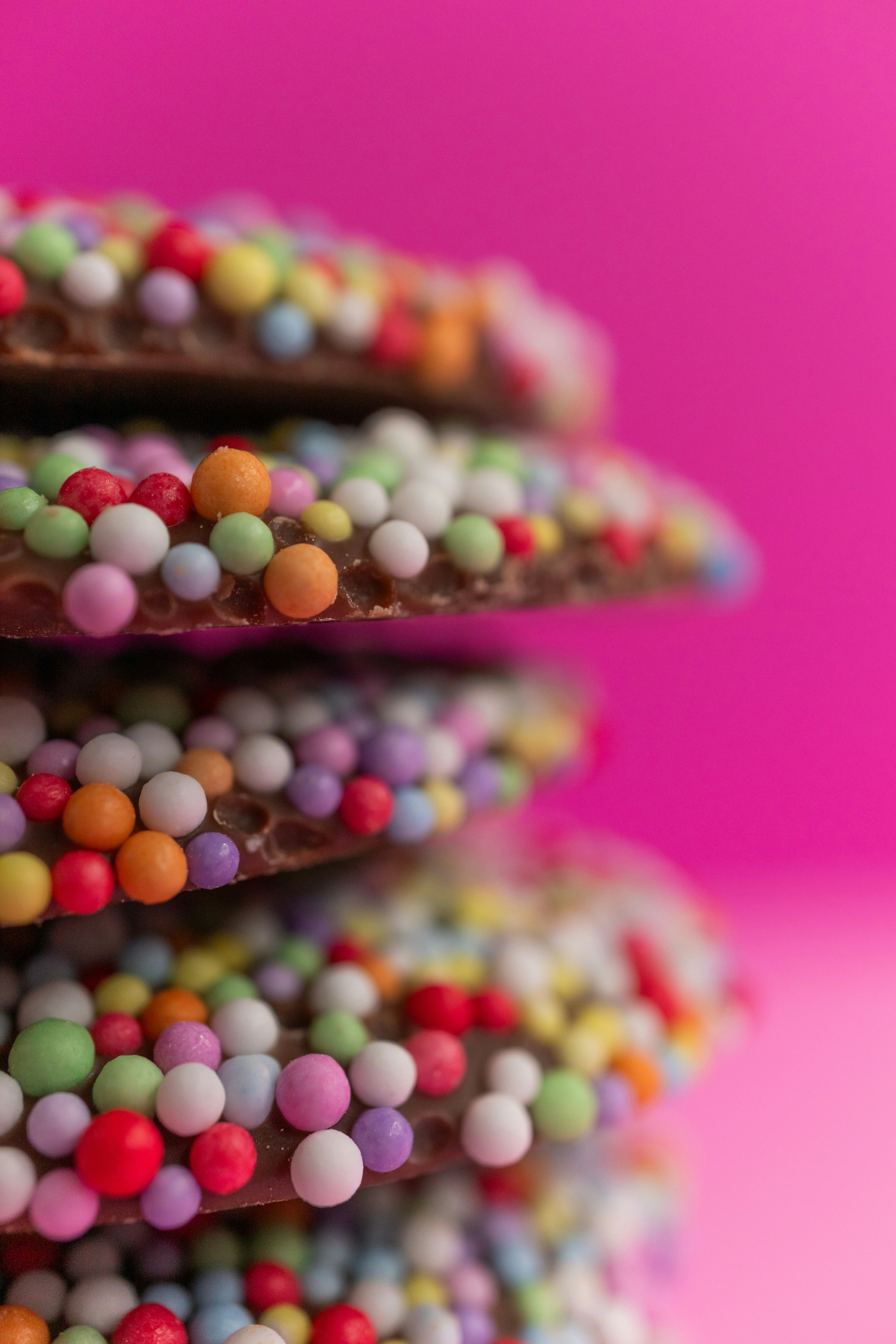 A stack of chocolate cookies covered in colorful sugar sprinkles against a pink background