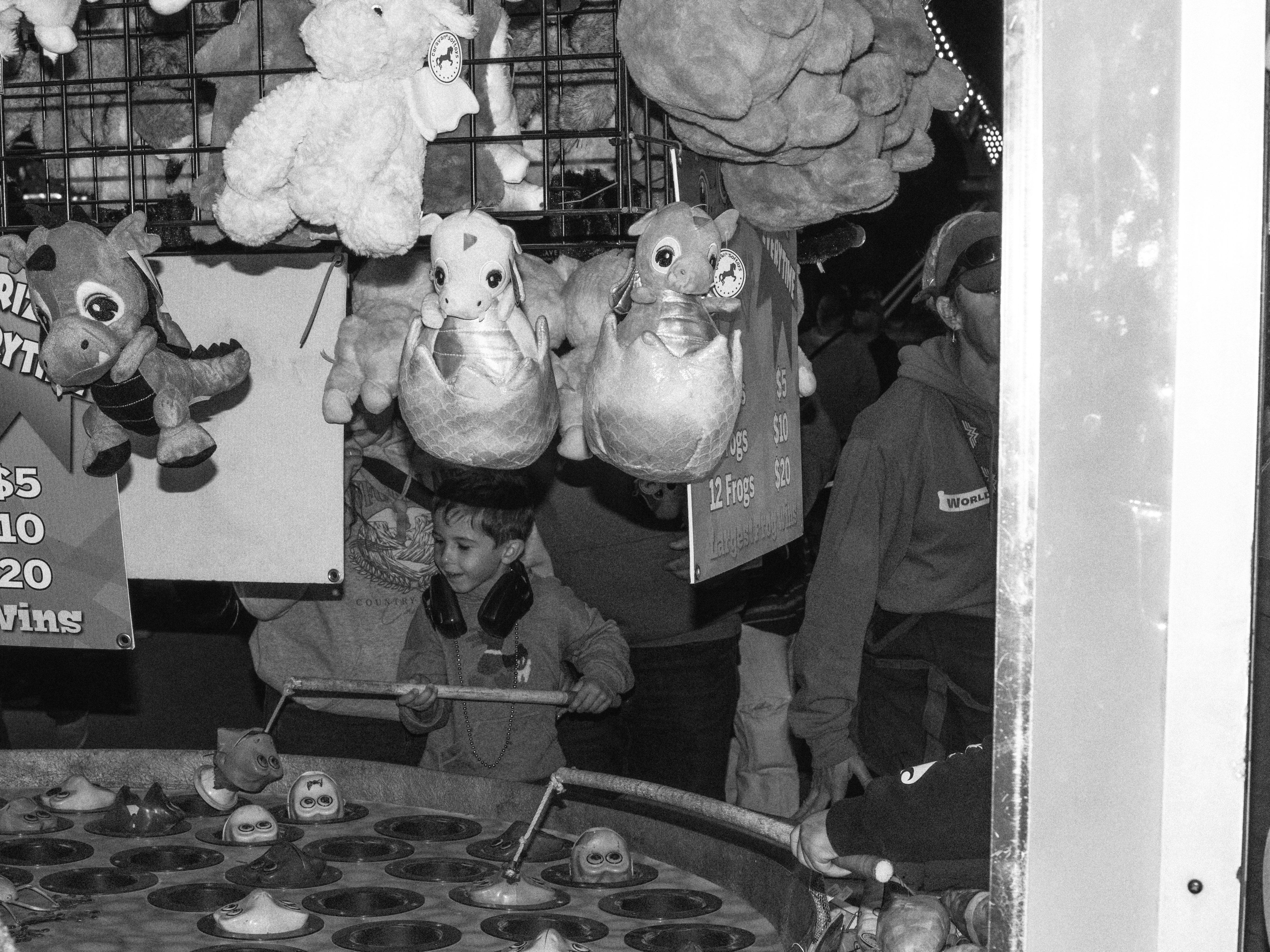 A child playing a carnival game with fishing rods and plush dragon prizes