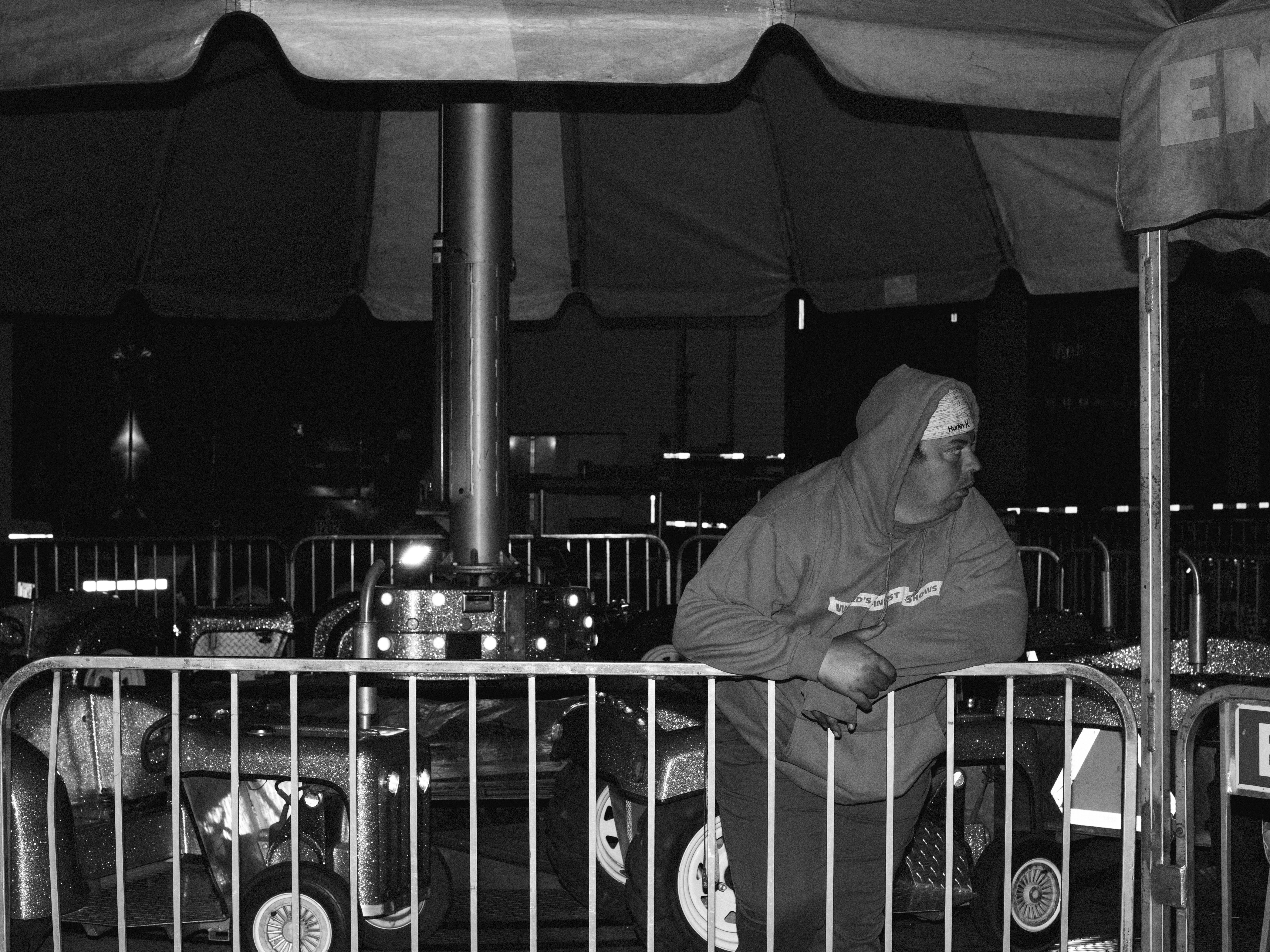 A person in a hooded sweatshirt leaning on a metal carnival ride fence