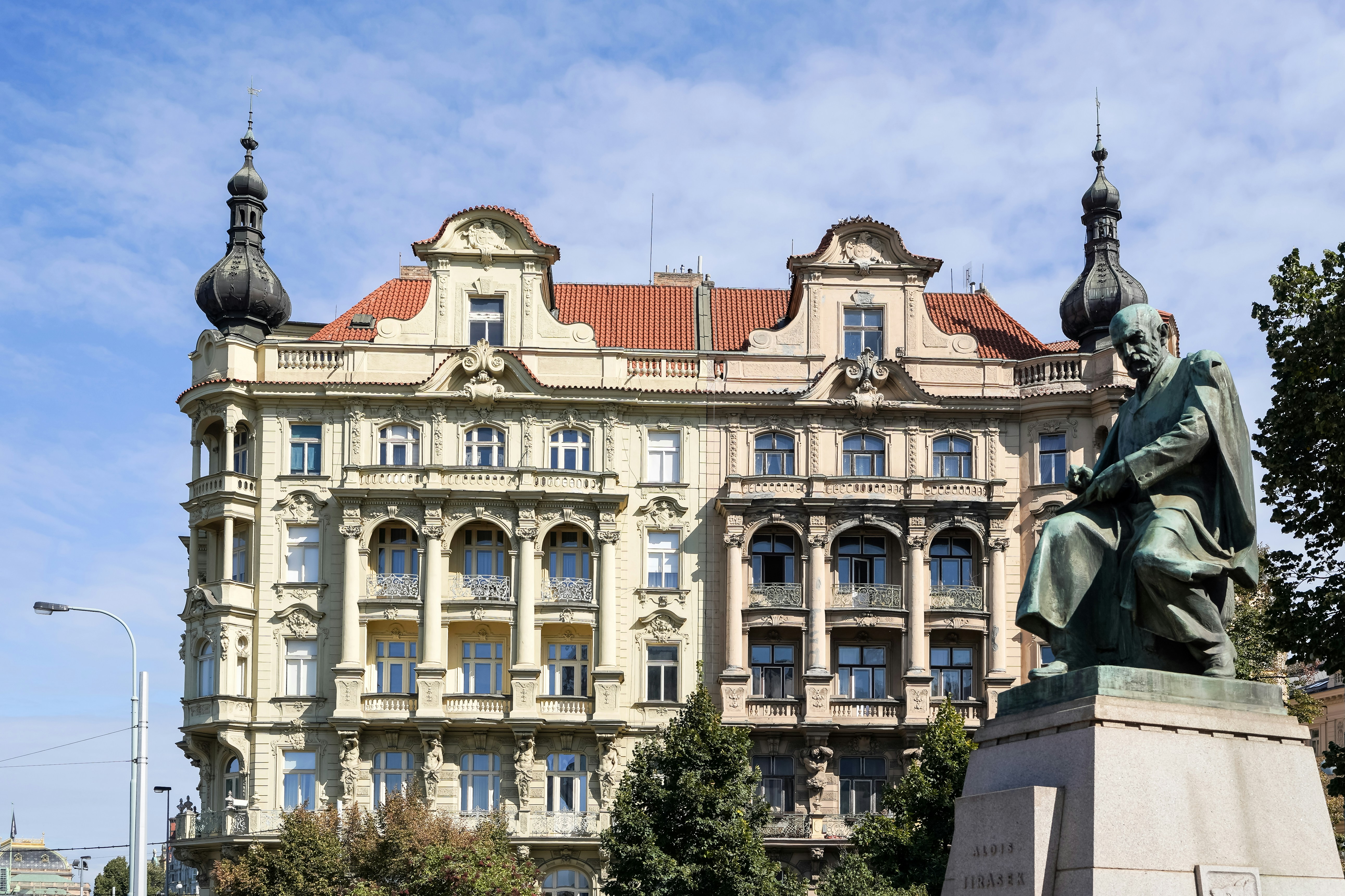 A bronze statue of a man seated before an ornate building in Prague