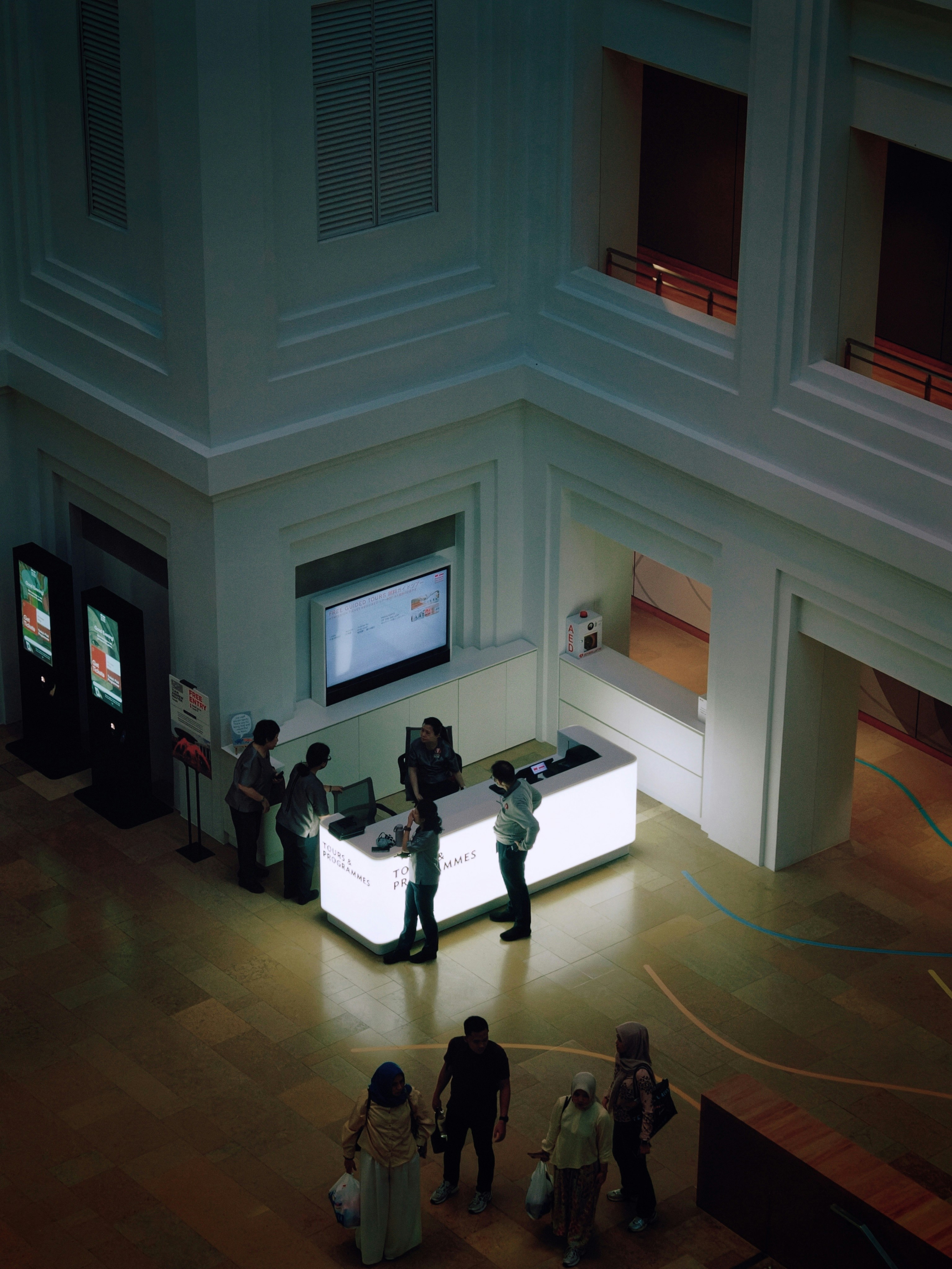 People at a glowing information desk in a large museum lobby - museum partnerships