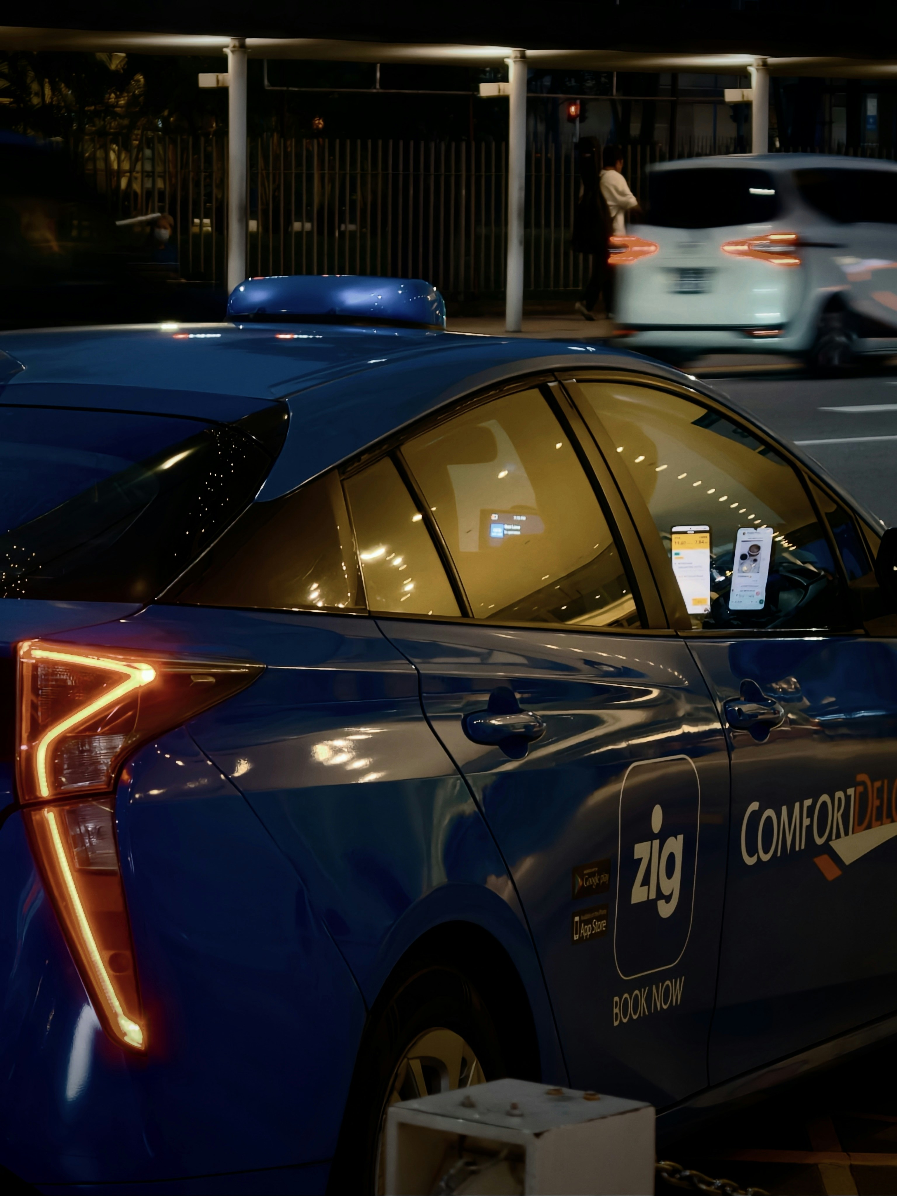 A blue taxi with illuminated taillights at night on a city street