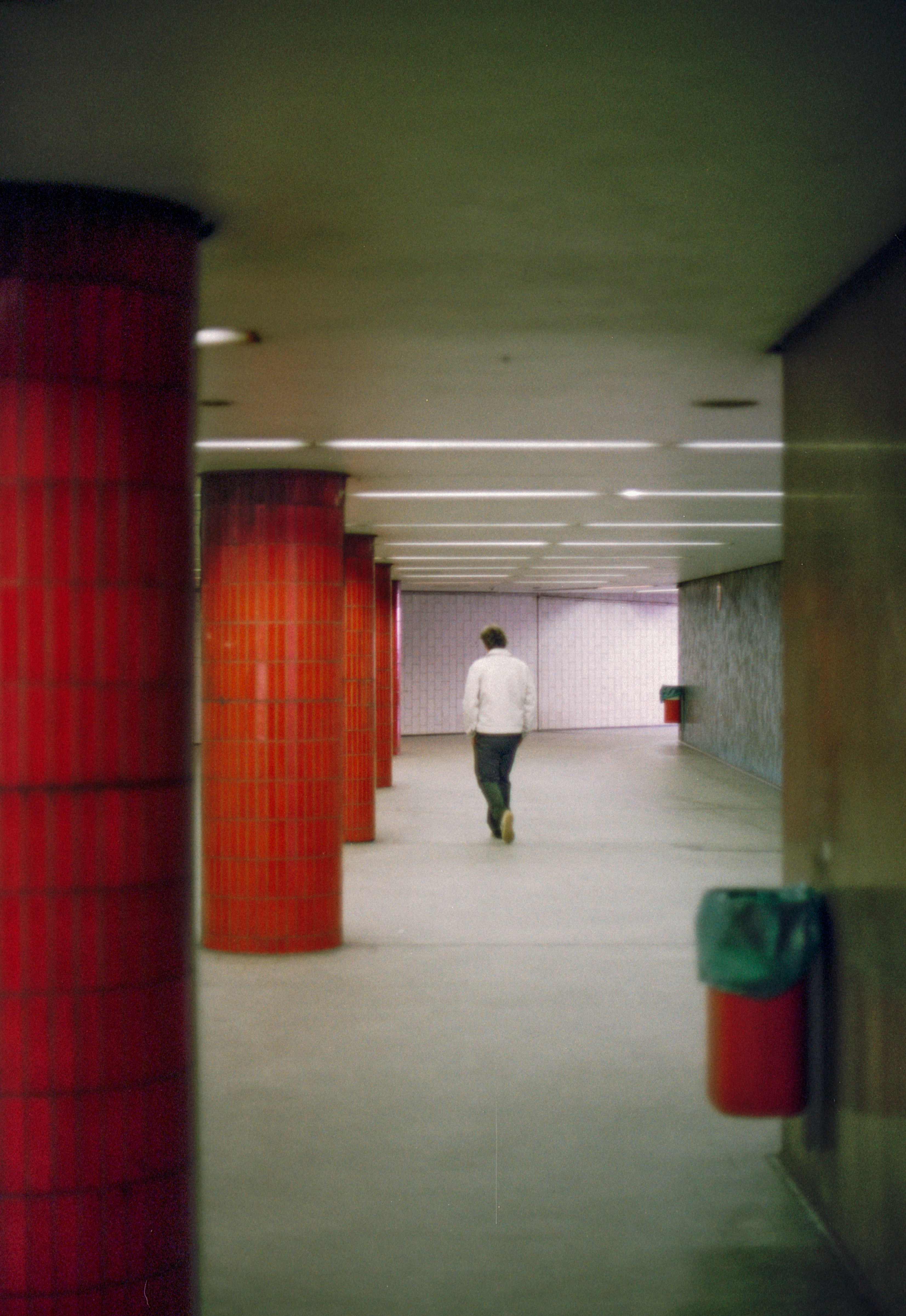 A person in a white jacket walking through a subway corridor with red pillars