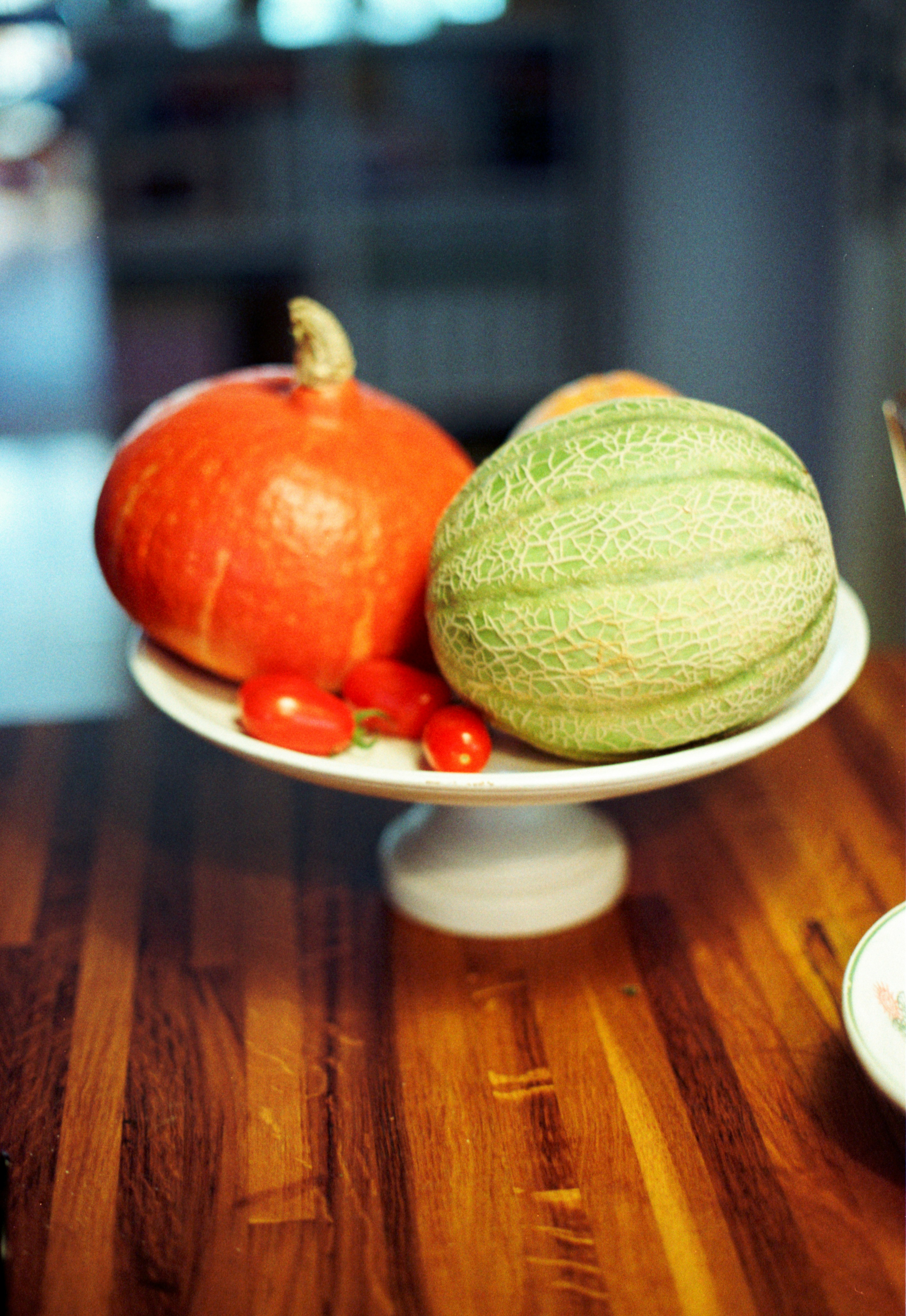 Ein Kürbis, eine Melone und Kirschtomaten auf einer weißen Sockelschale