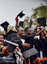 A group of graduates in black robes and caps celebrating in the rain