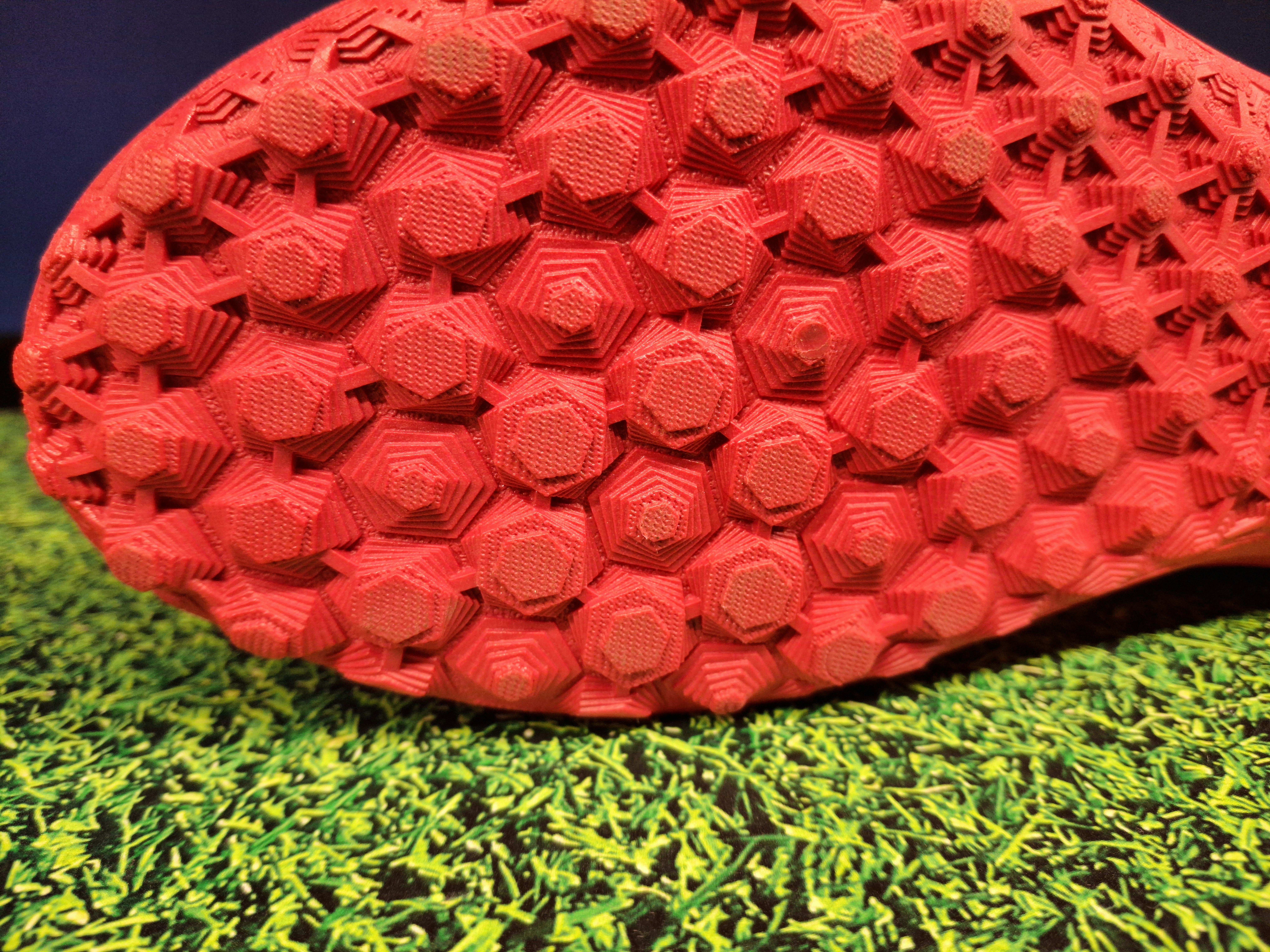 The red textured sole of a soccer cleat above green artificial turf