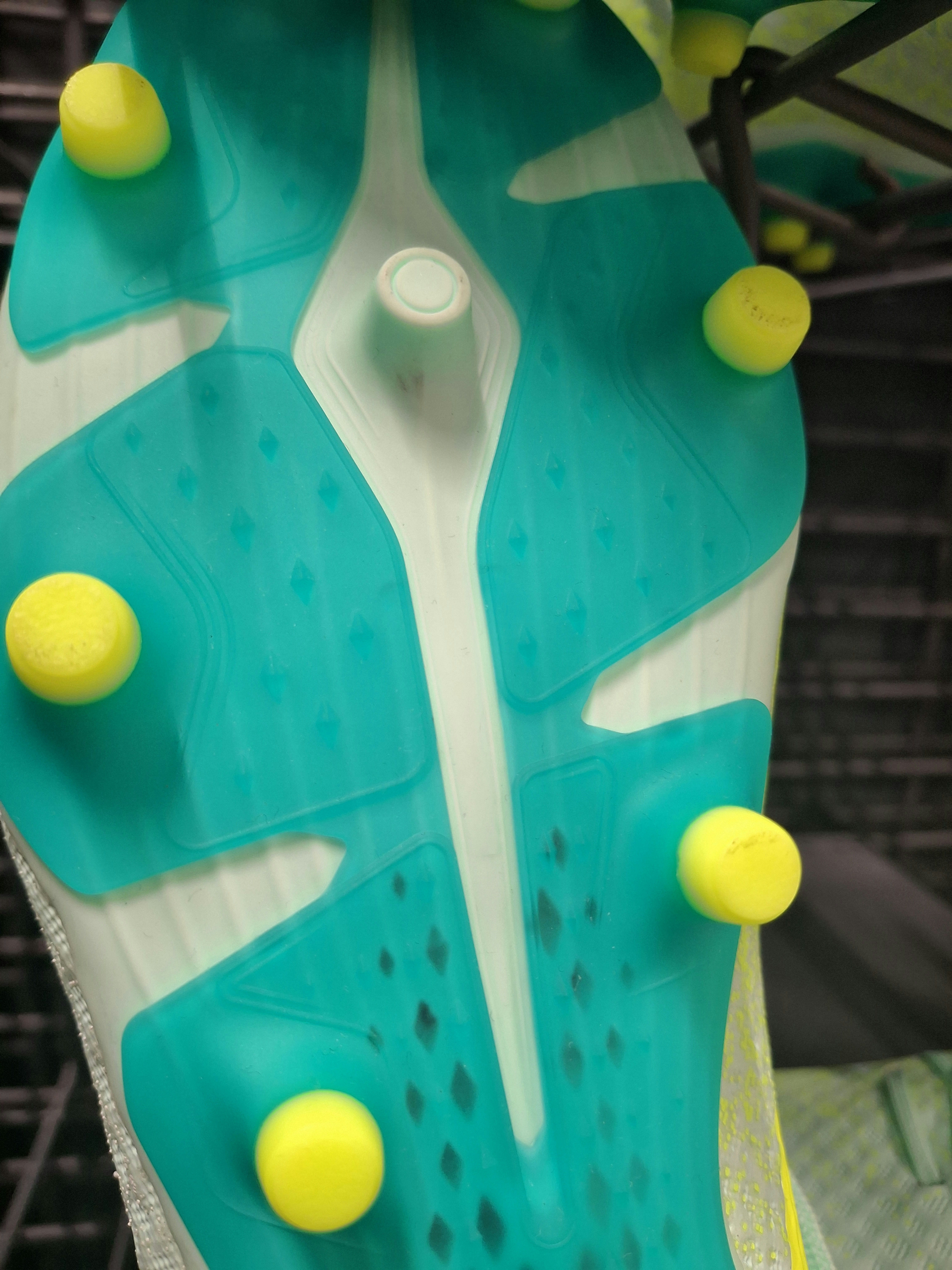 The sole of a soccer cleat with bright yellow studs on teal plates