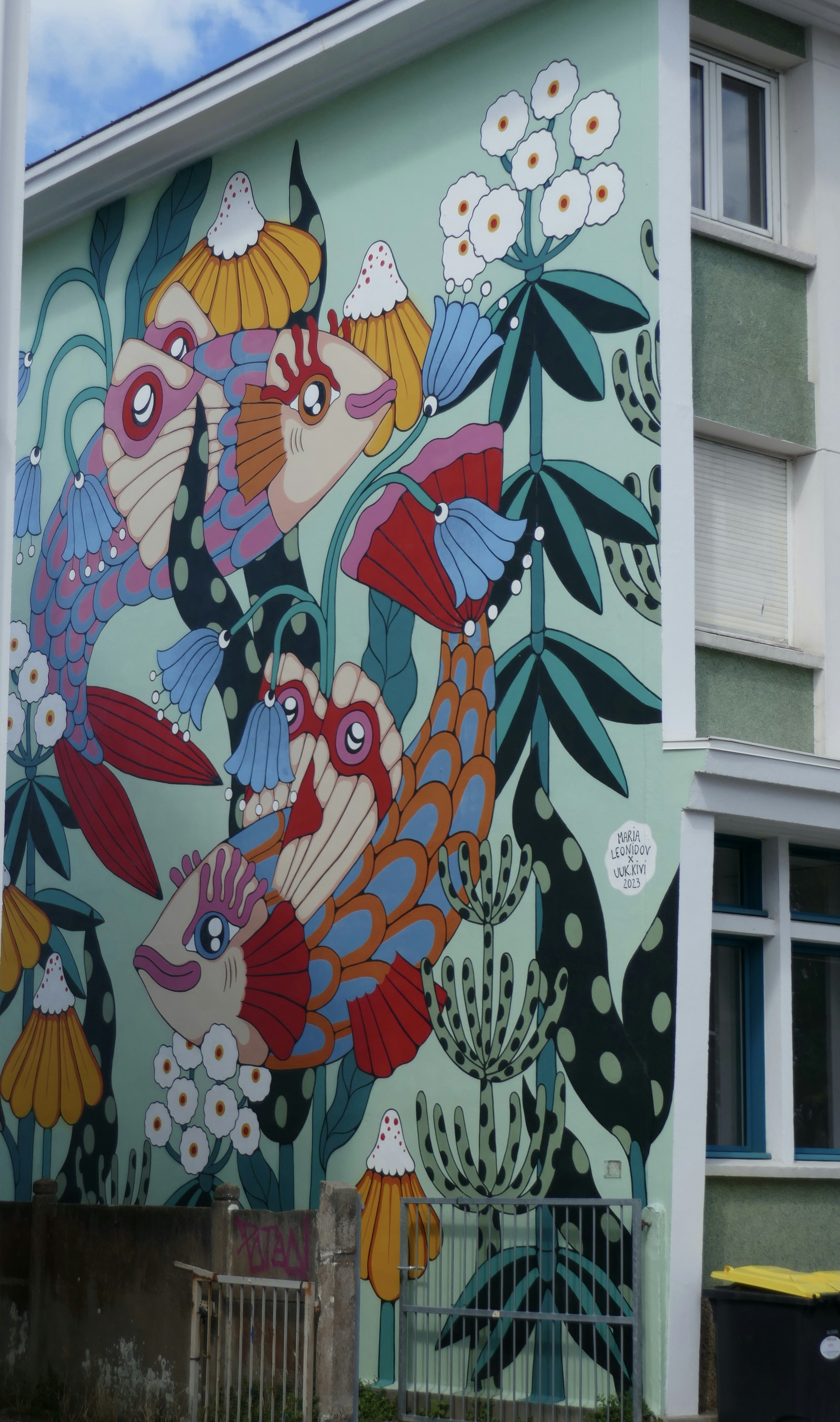 A colorful mural of stylized fish and flowers on a light green building wall
