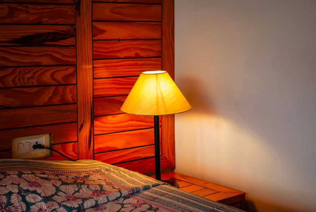 A bed with floral bedding beside a lit table lamp