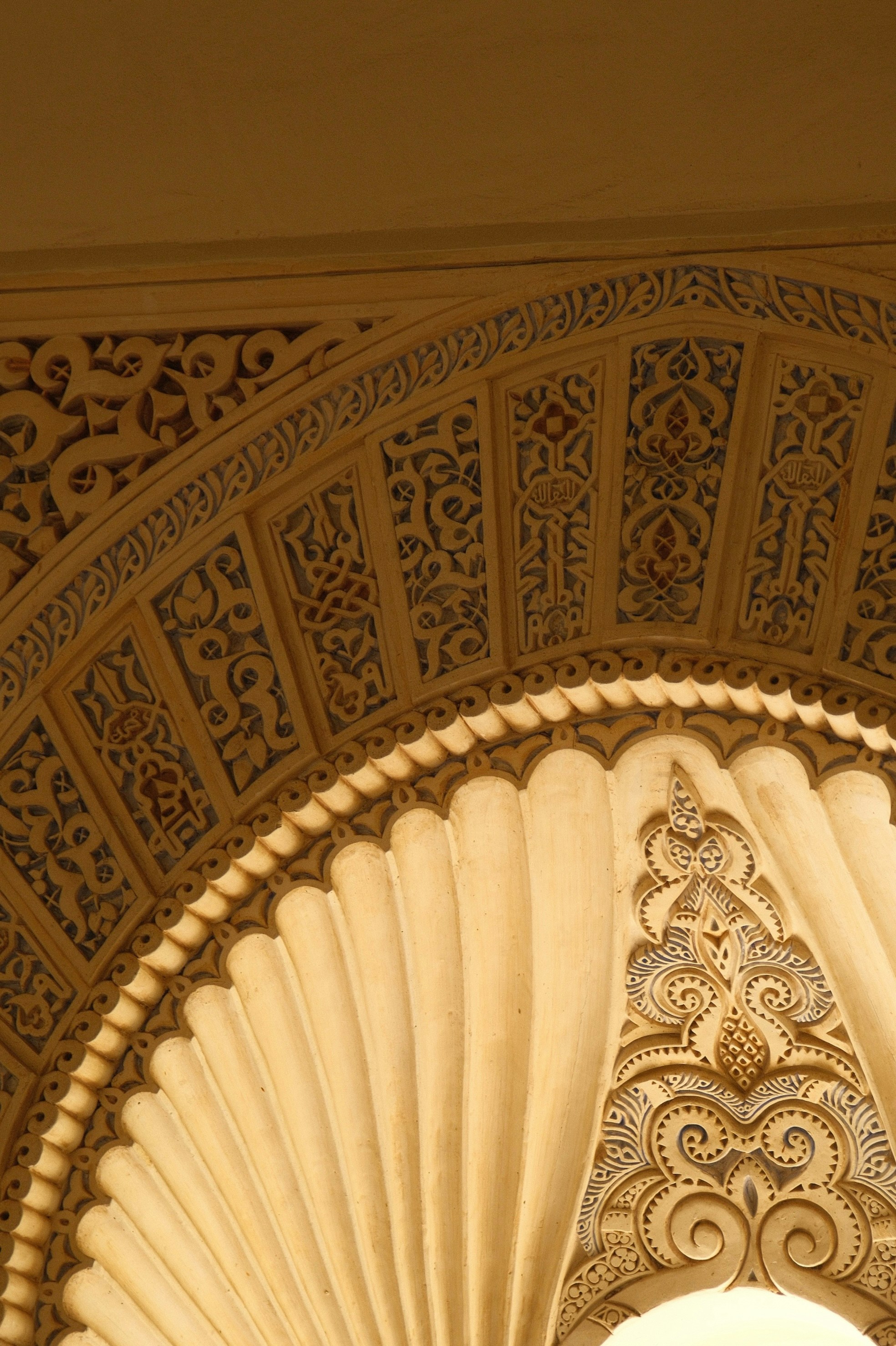 Arco in gesso intagliato con motivi geometrici e calligrafia araba in caldi tonalità beige