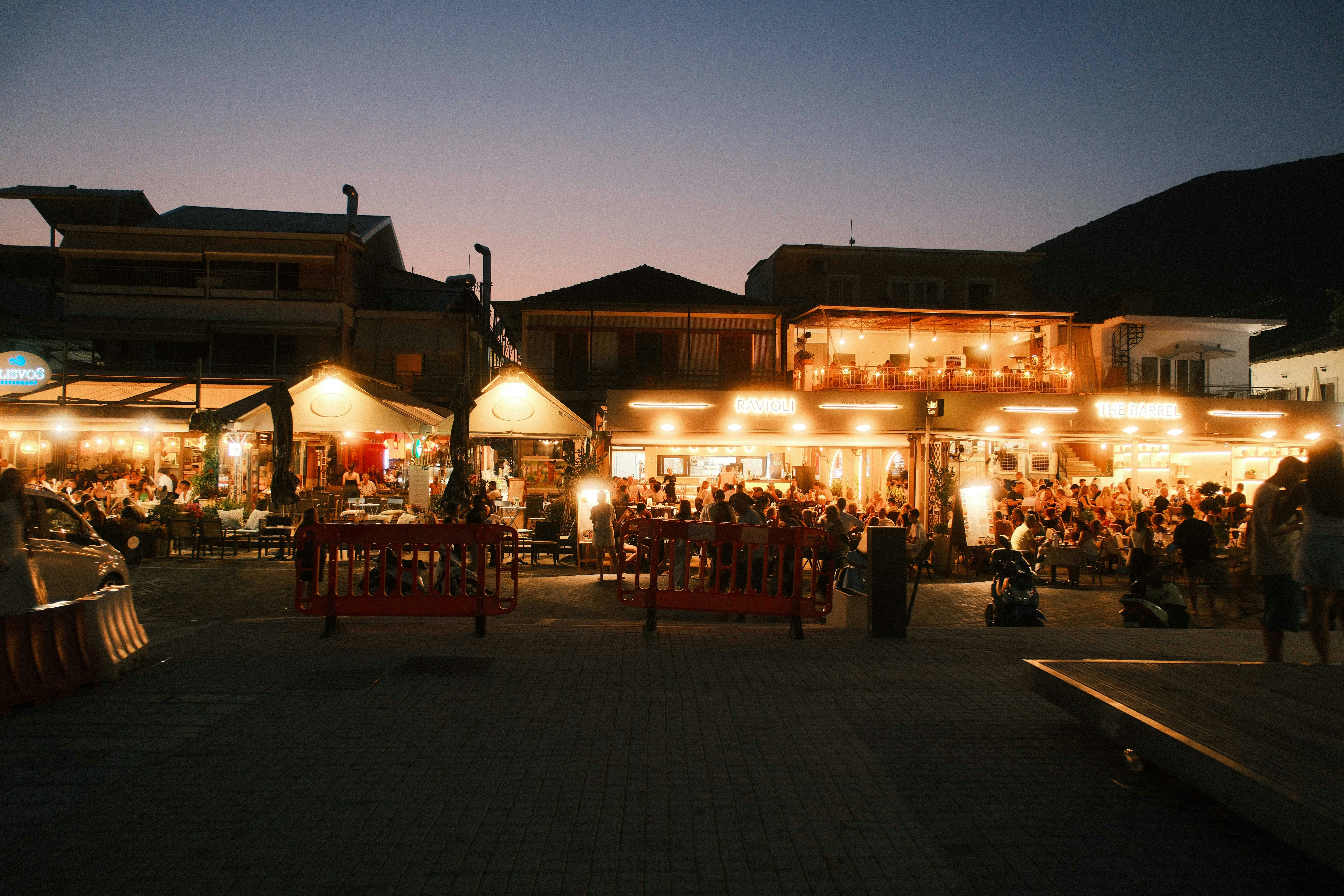 People dining at outdoor restaurants with glowing lights at dusk