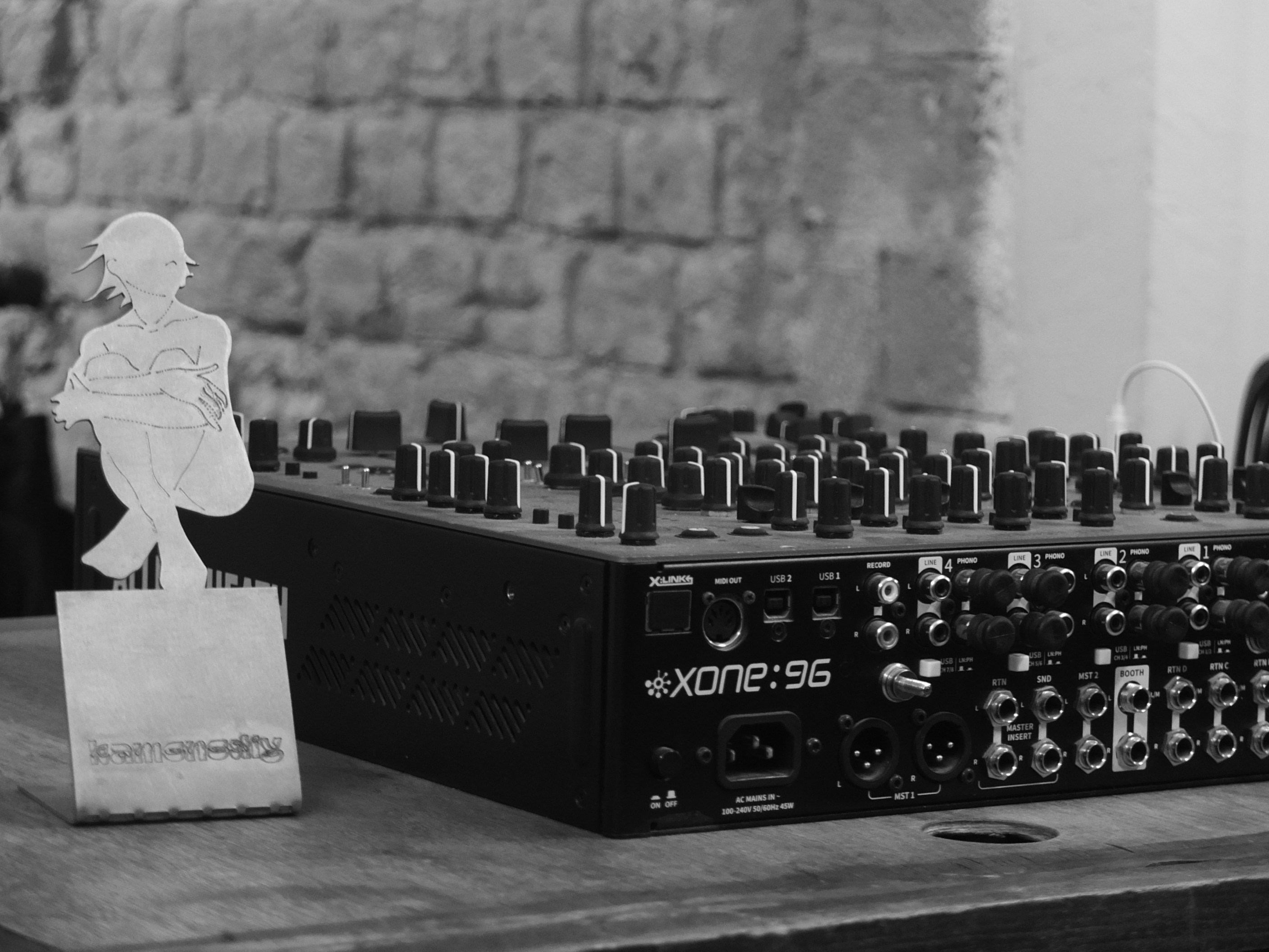 A black audio mixer beside a small metal figure on a wooden table