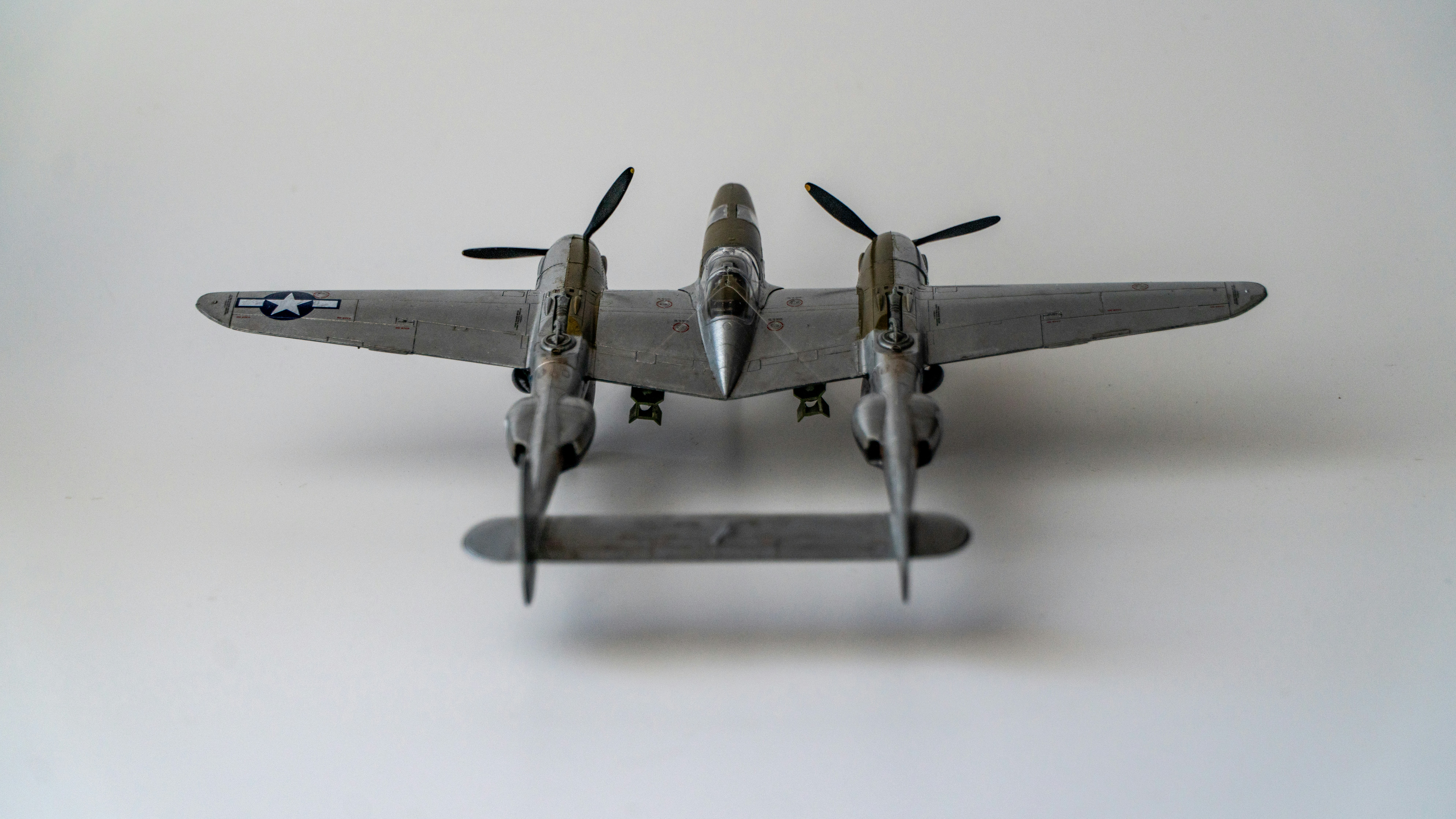 Un modèle d’avion P-38 Lightning argenté avec deux hélices sur une surface blanche
