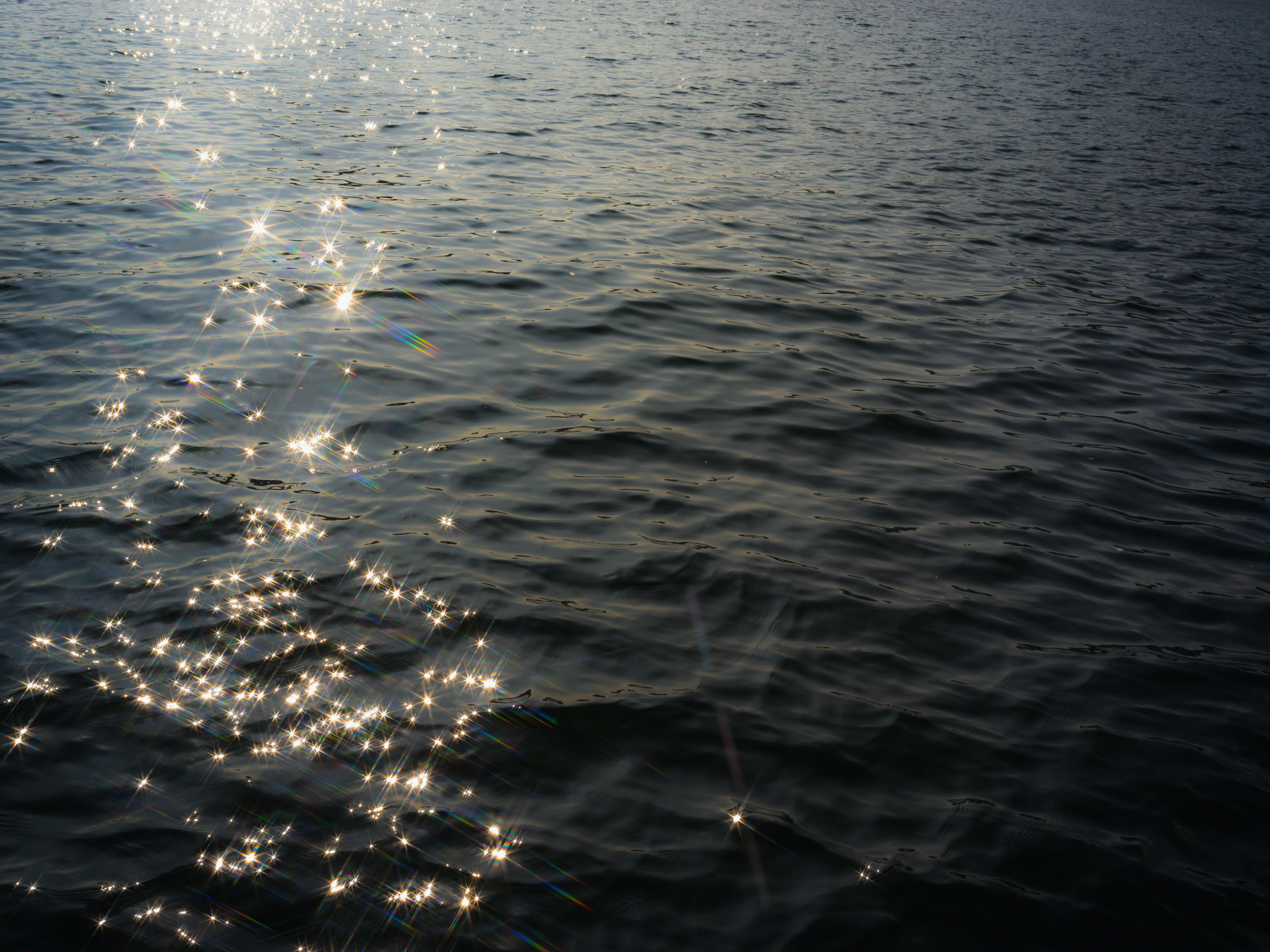 Sunlight reflecting off dark rippling water creating bright star-shaped glints