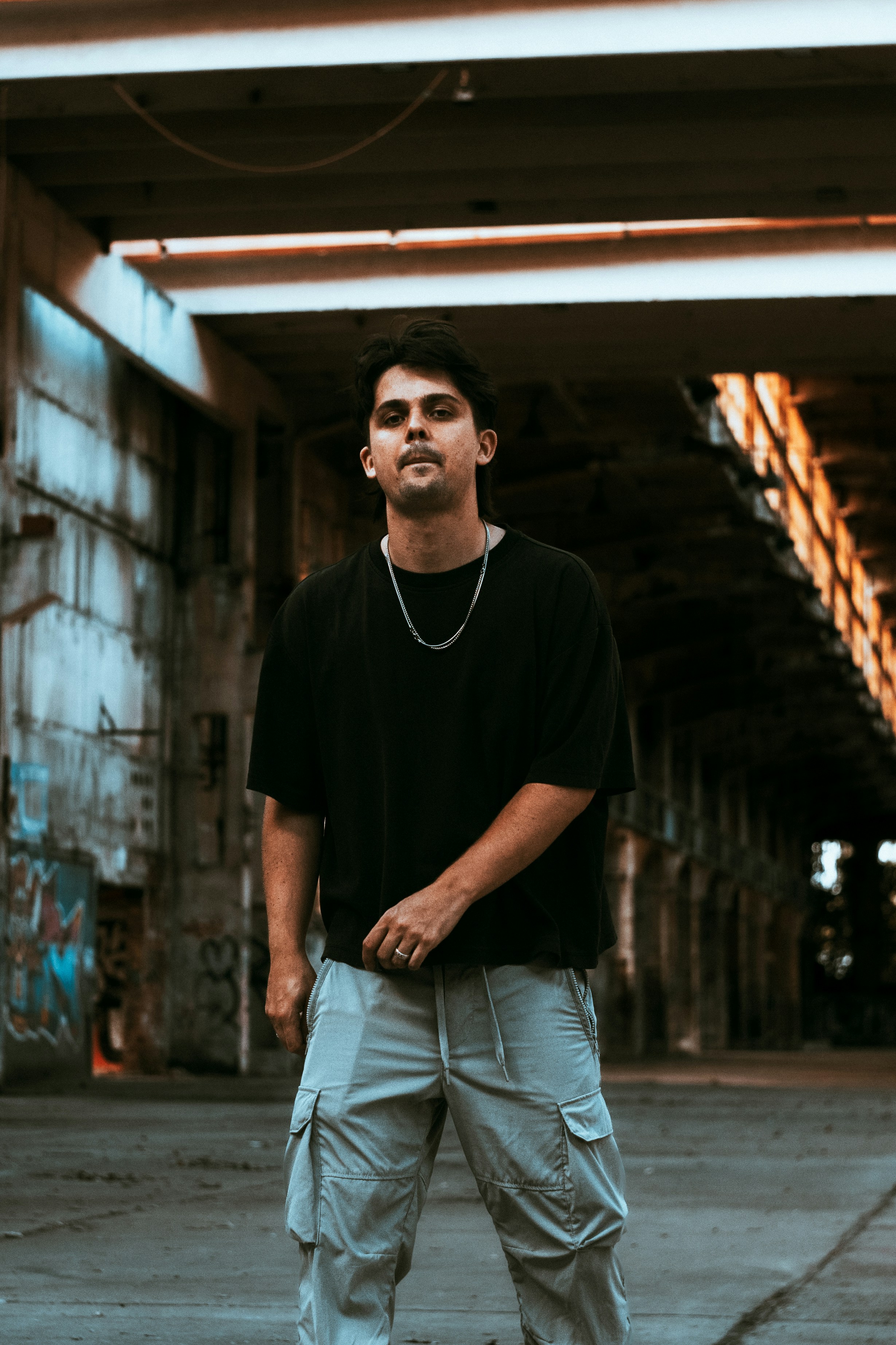 A man in a black t-shirt and grey cargo pants in an industrial warehouse