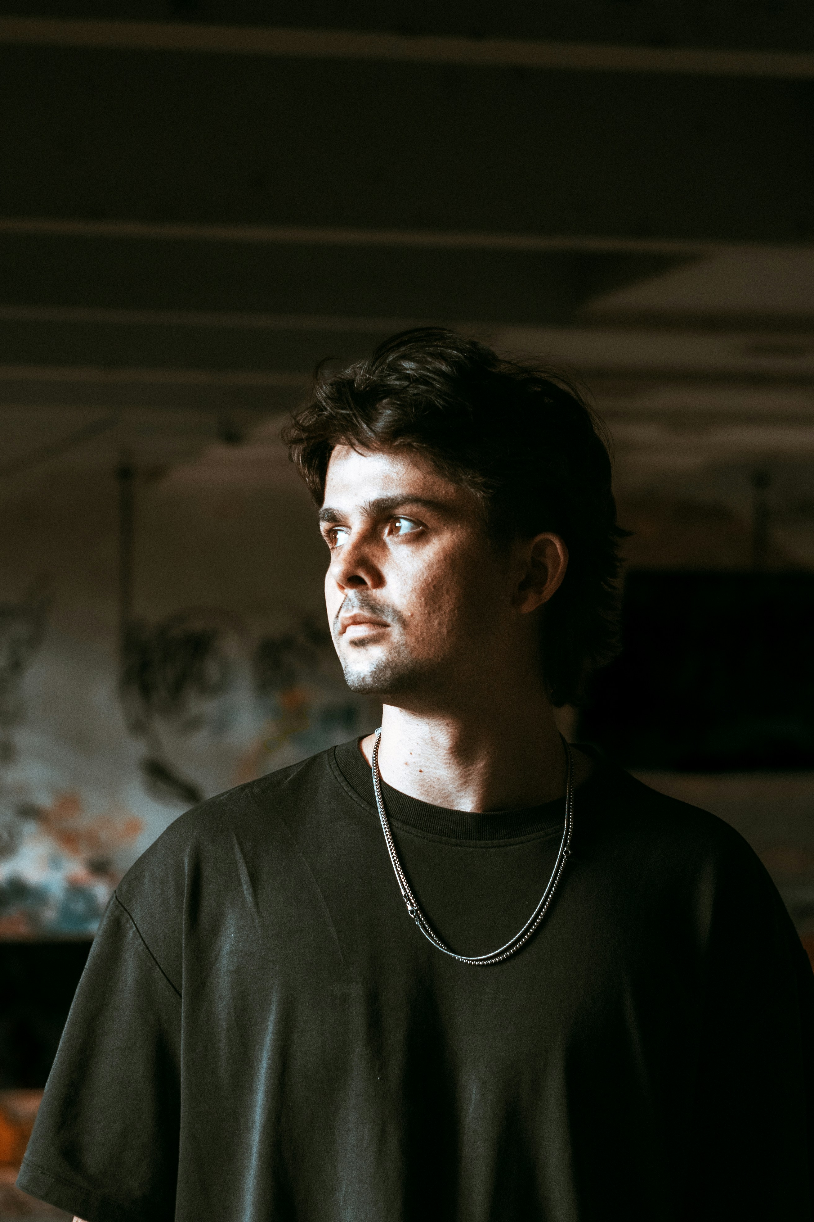 A man with dark hair wearing a black t-shirt and silver chain