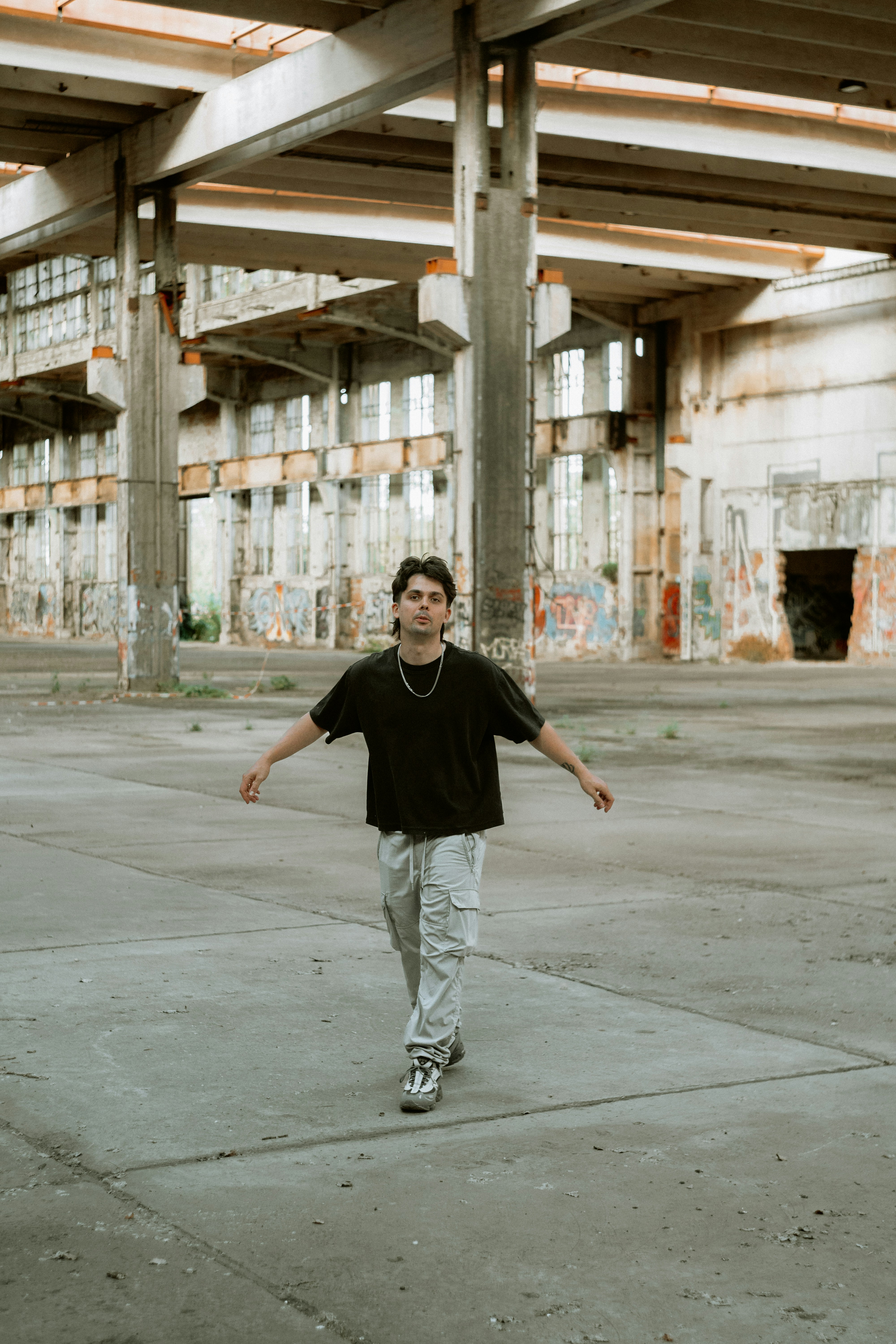 A man in a black t-shirt walking through an abandoned warehouse