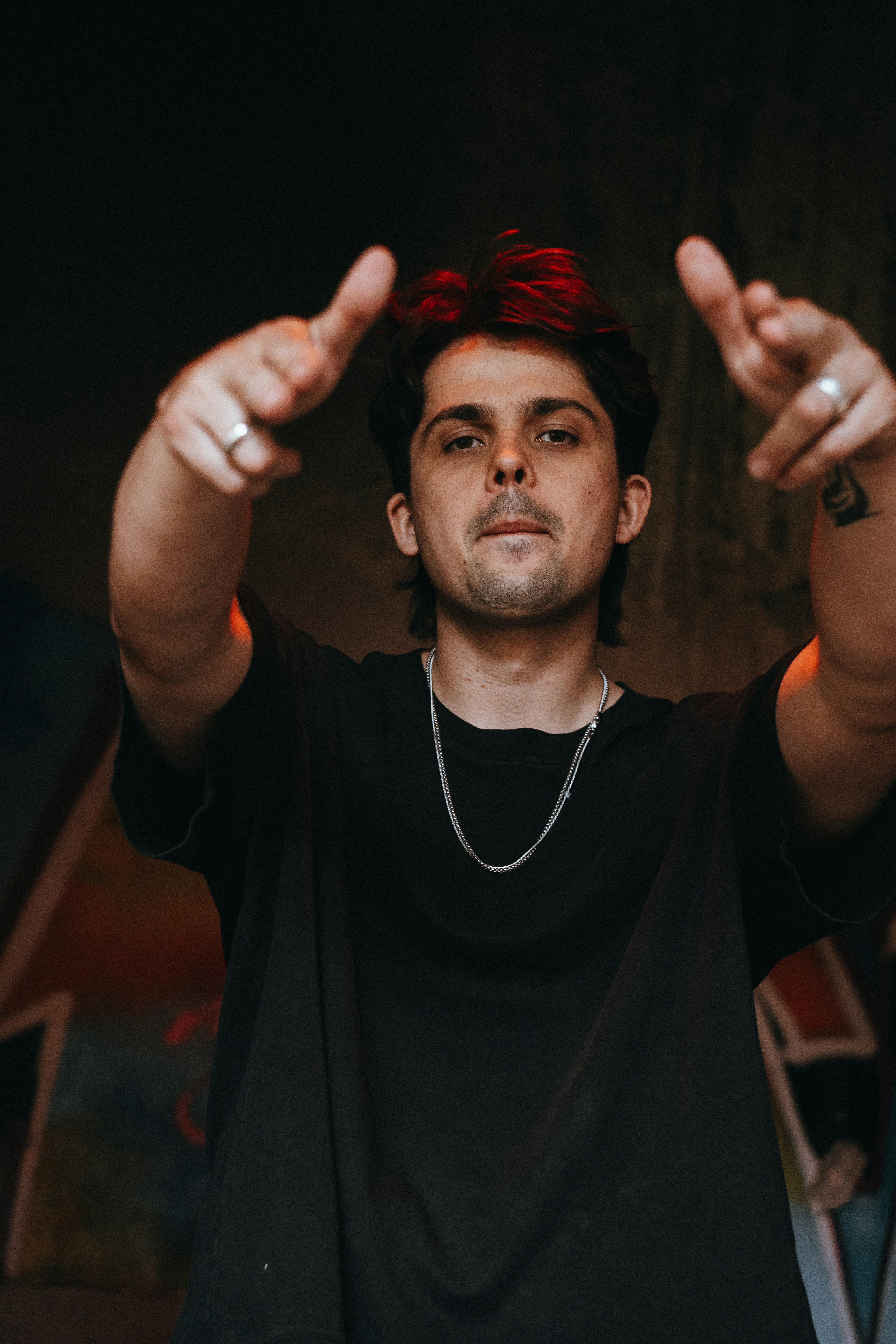 A man in a black t-shirt pointing forward with both hands in dim light
