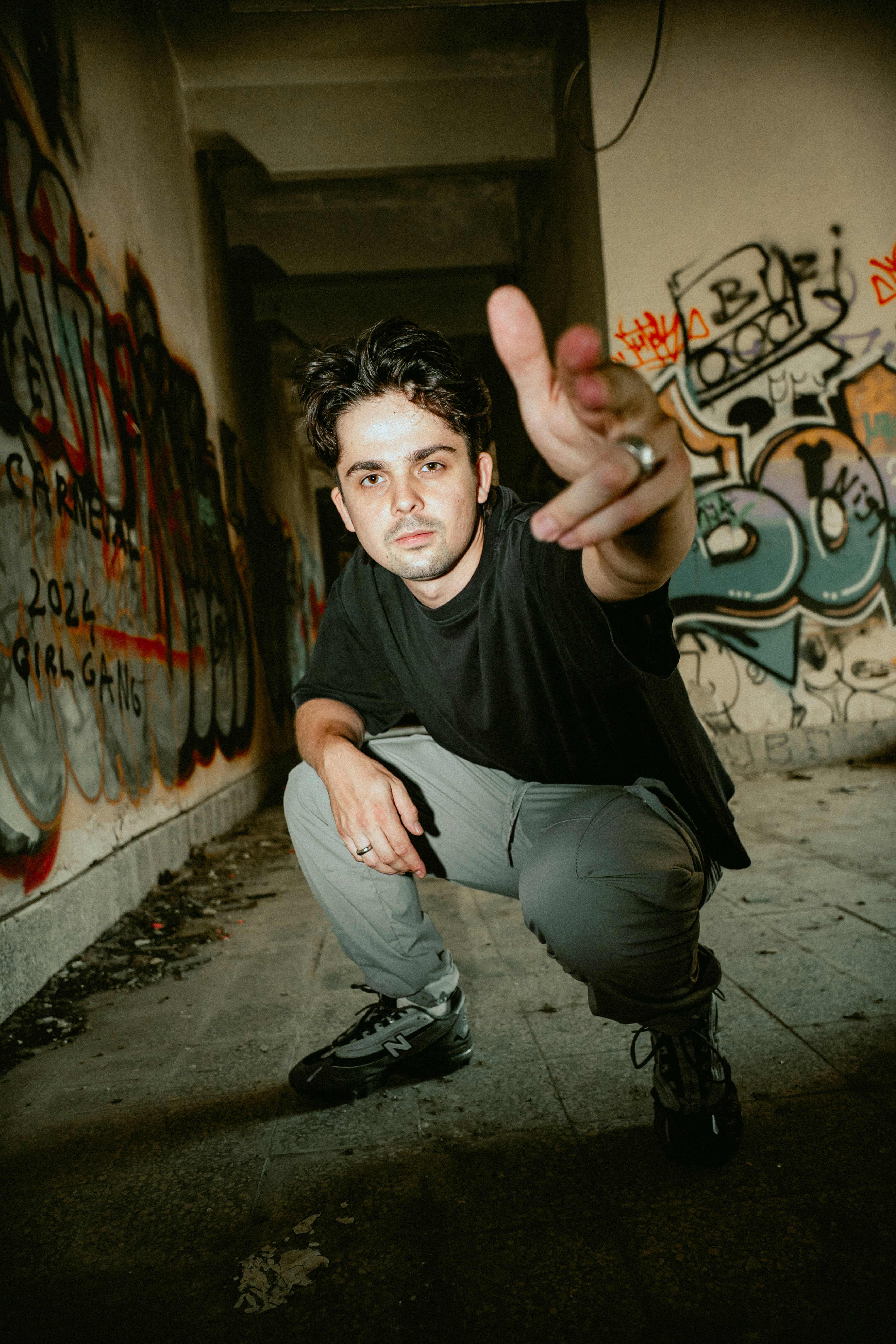 A man in a black t-shirt crouching in a graffiti-covered hallway