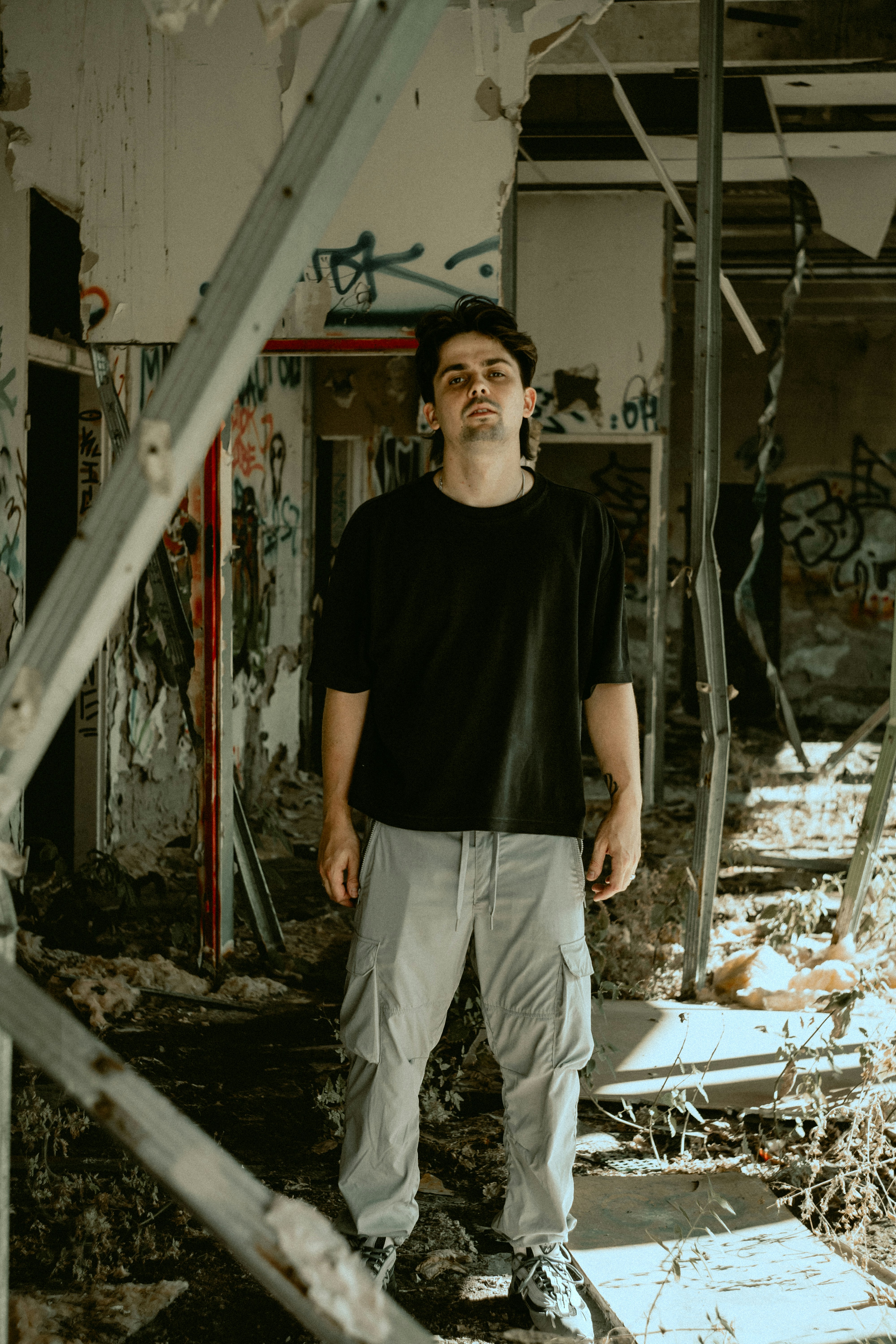 A man in a black t-shirt and grey cargo pants in a derelict building