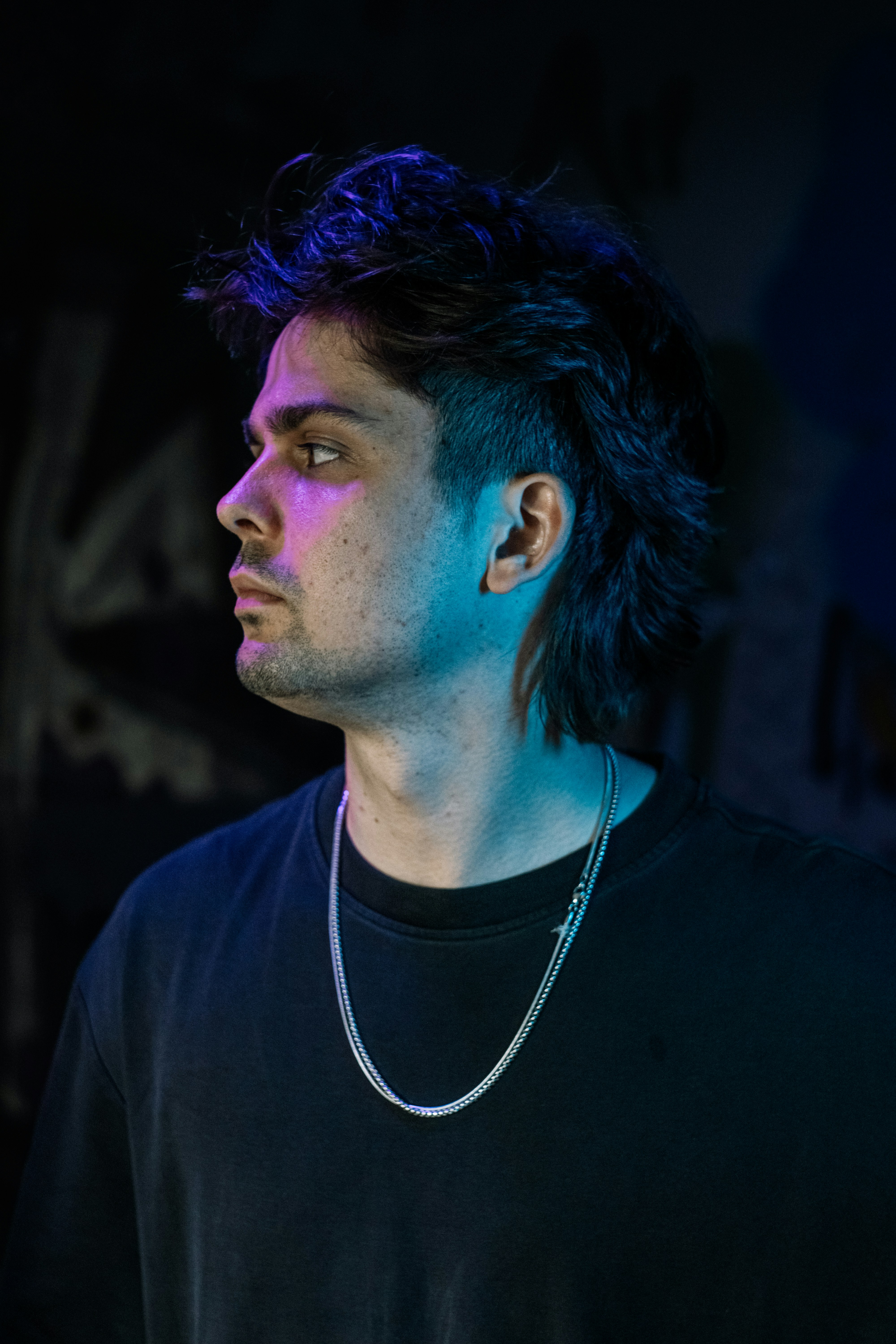 A man with a mullet wearing a silver chain in blue and purple light