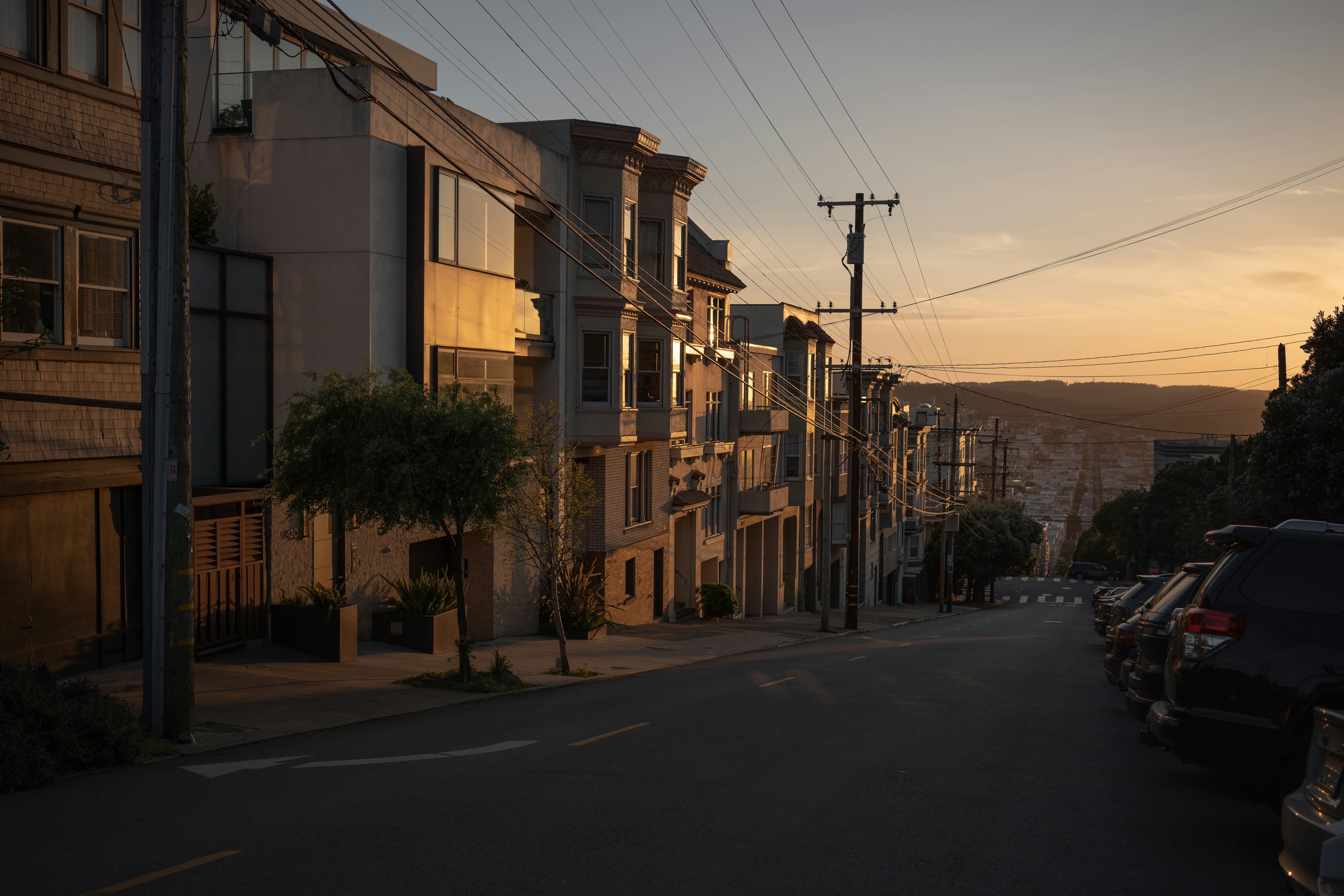 A steep street in San Francisco lined with apartment buildings during golden hour