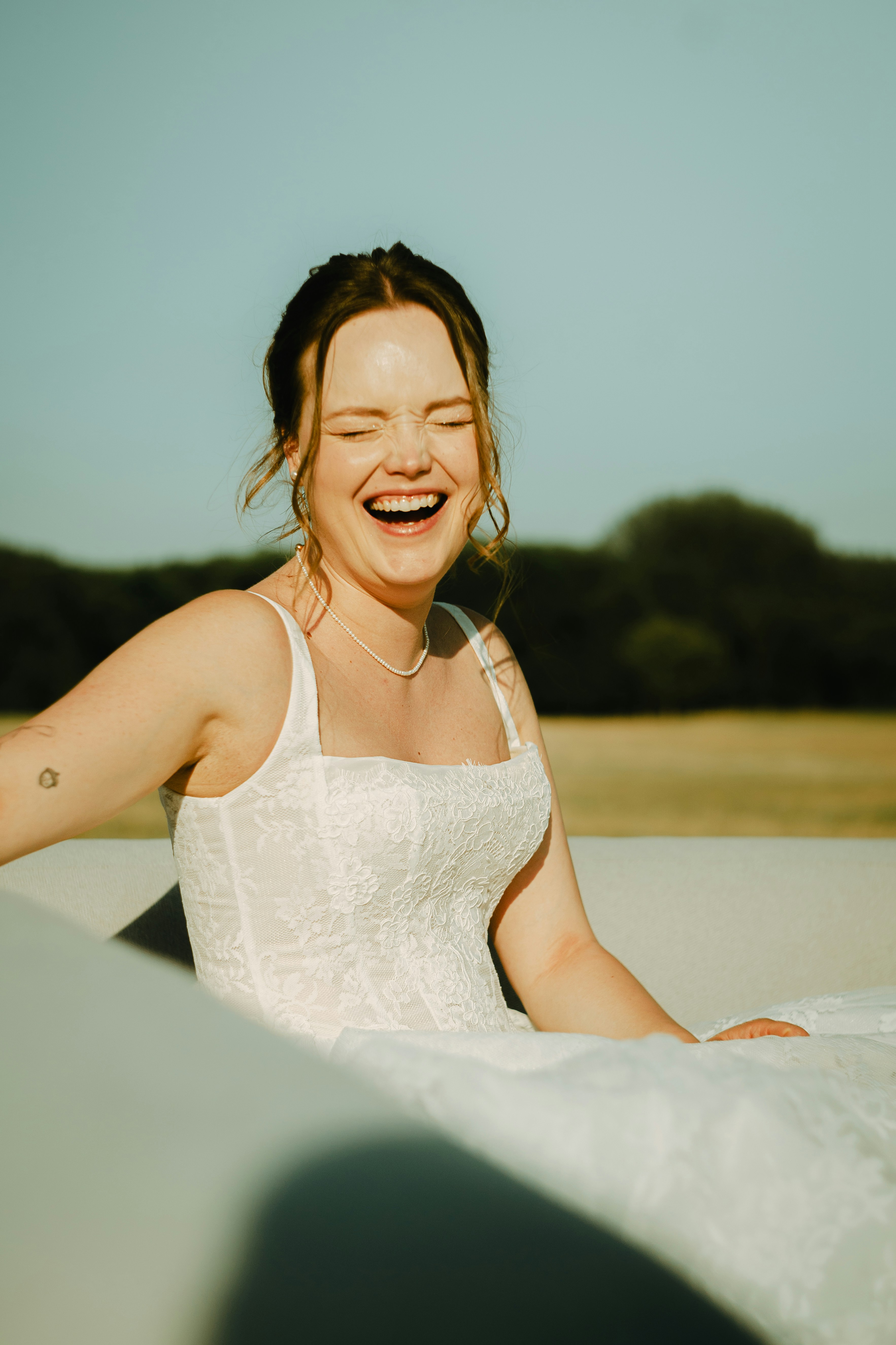 A woman in a white lace wedding dress laughing outdoors in golden light